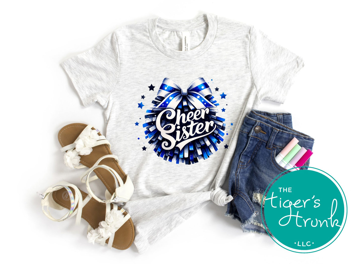 White t-shirt with 'Cheer Sister' design, sandals, shorts, and stationery on a white background with 'The Tiger's Trunk' logo.