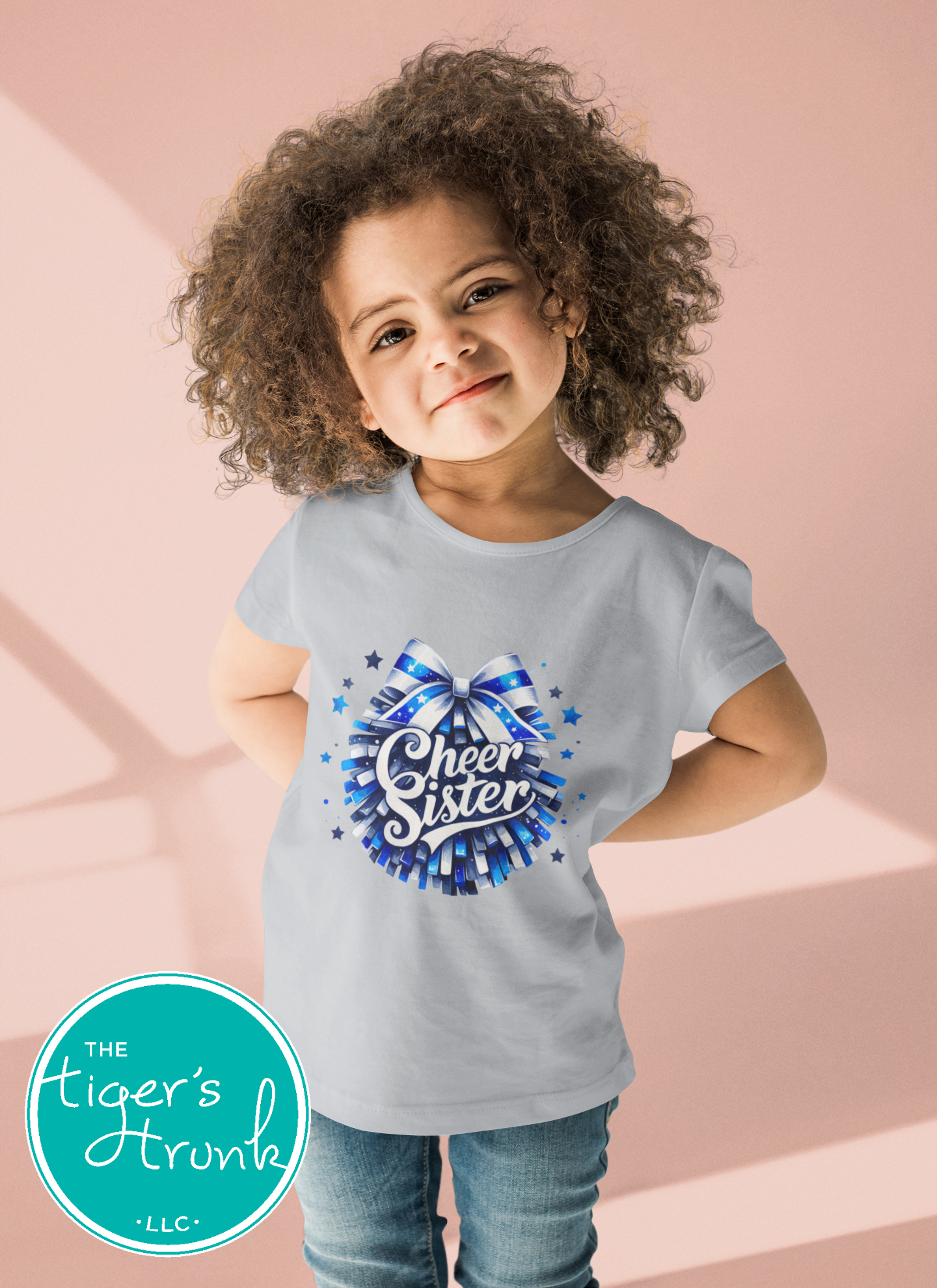 Child wearing a light blue t-shirt with 'Cheer Sister' design, standing against a pink background.