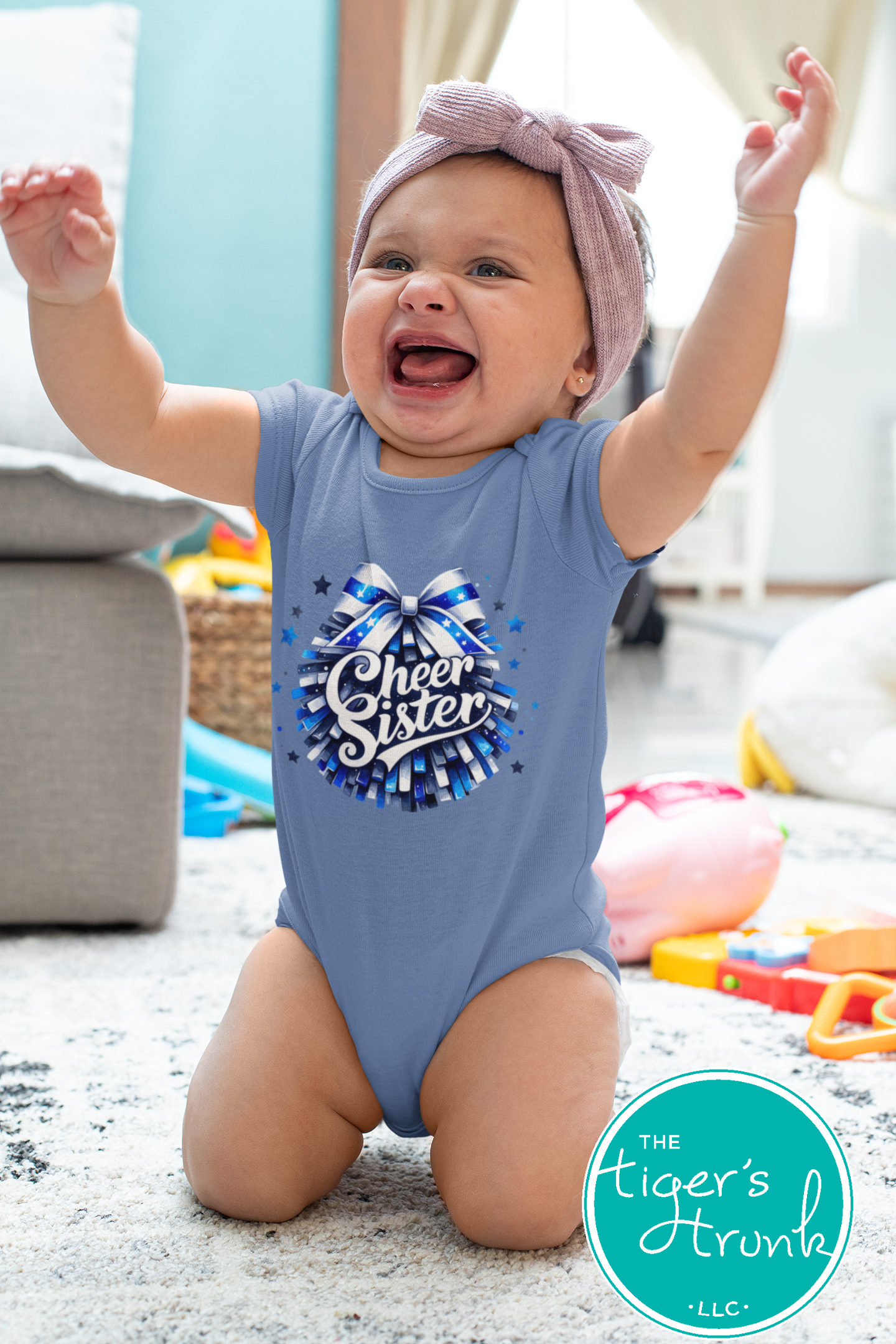 Baby wearing a blue onesie with 'Cheer Sister' text and a bow graphic, sitting on a carpeted floor.