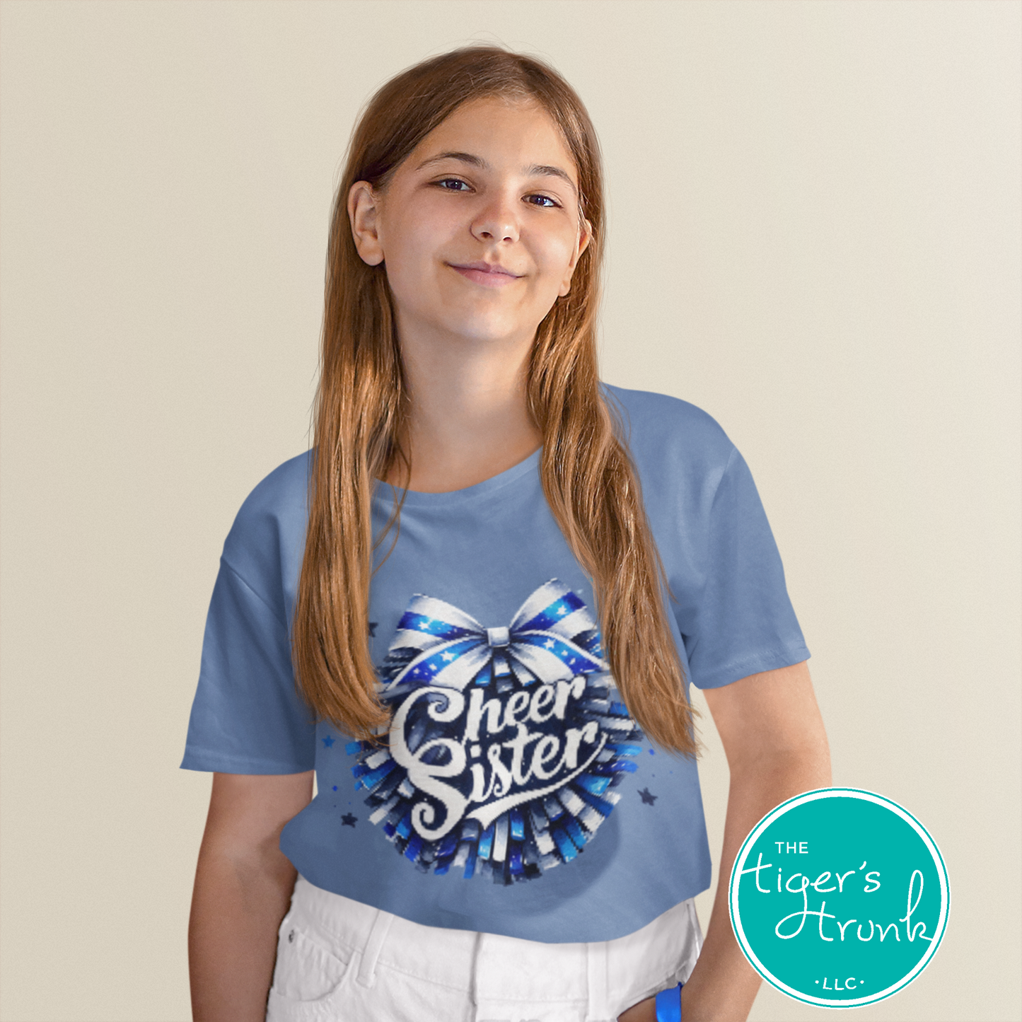 Girl wearing a blue t-shirt with 'Cheer Sister' design, standing against a beige background.