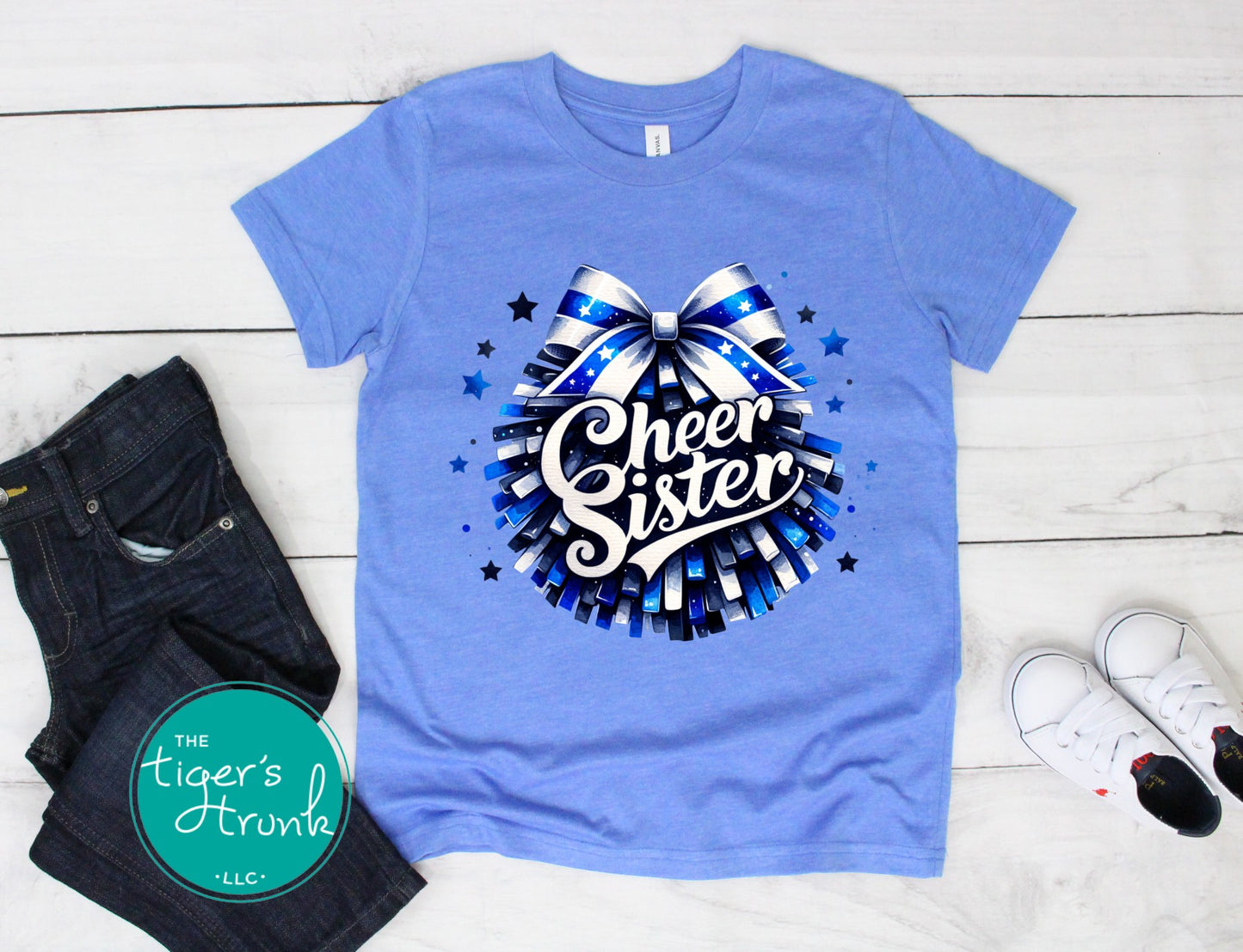 Blue t-shirt with 'Cheer Sister' design on a wooden floor with jeans and sneakers.