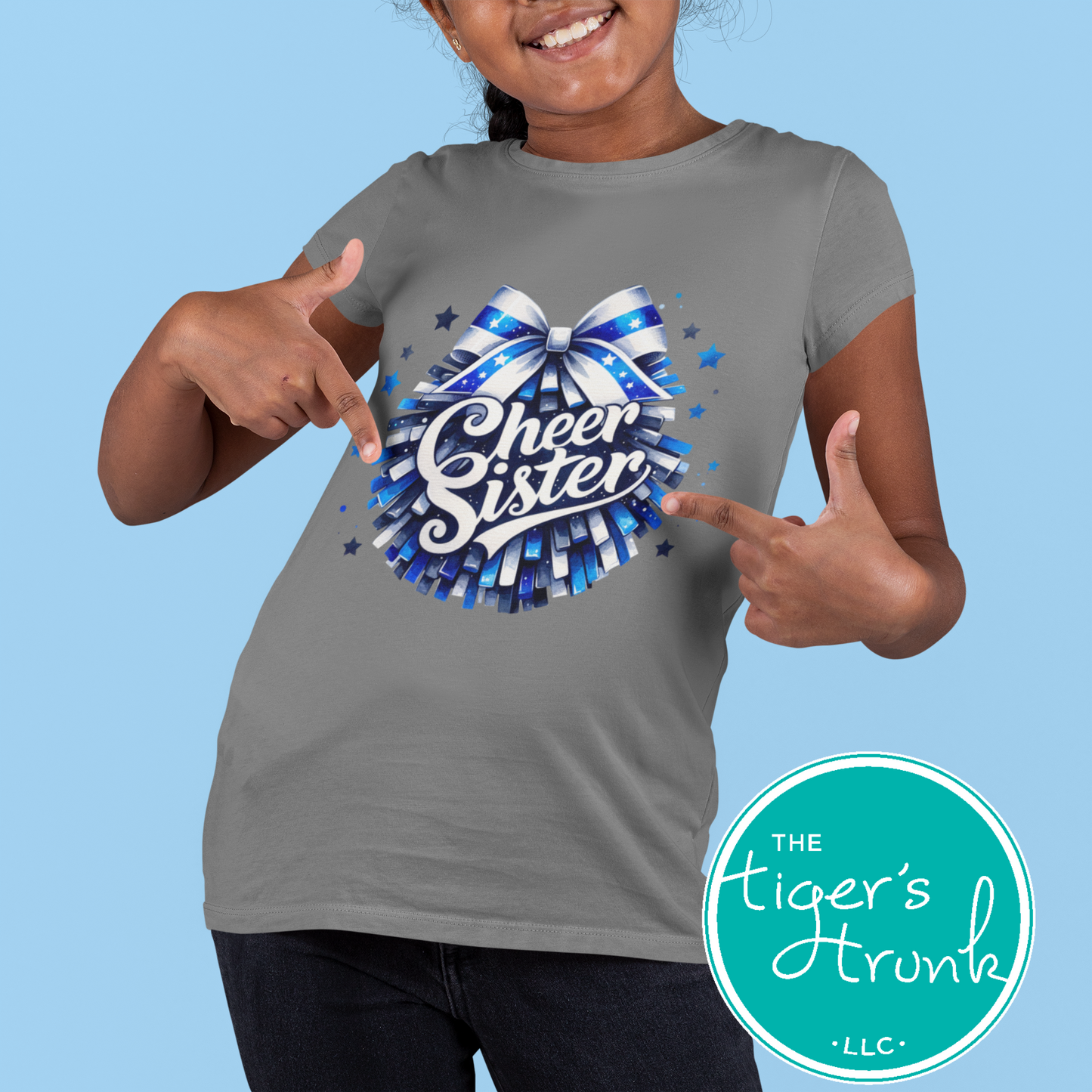 Child wearing a gray t-shirt with 'Cheer Sister' design, pointing at the shirt against a blue background.