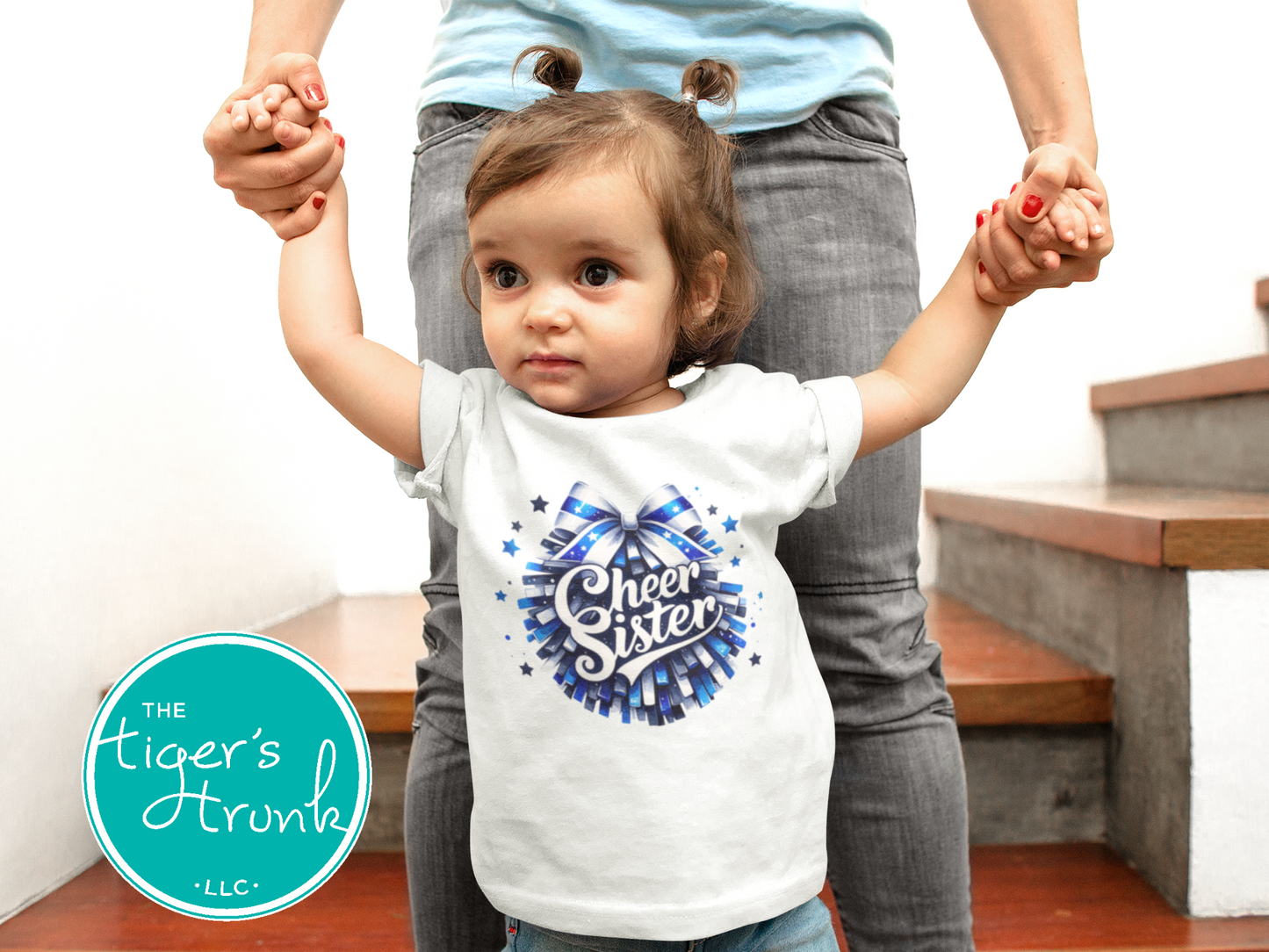 Child wearing a 'Cheer Sister' t-shirt with an adult standing behind them, holding their hands.