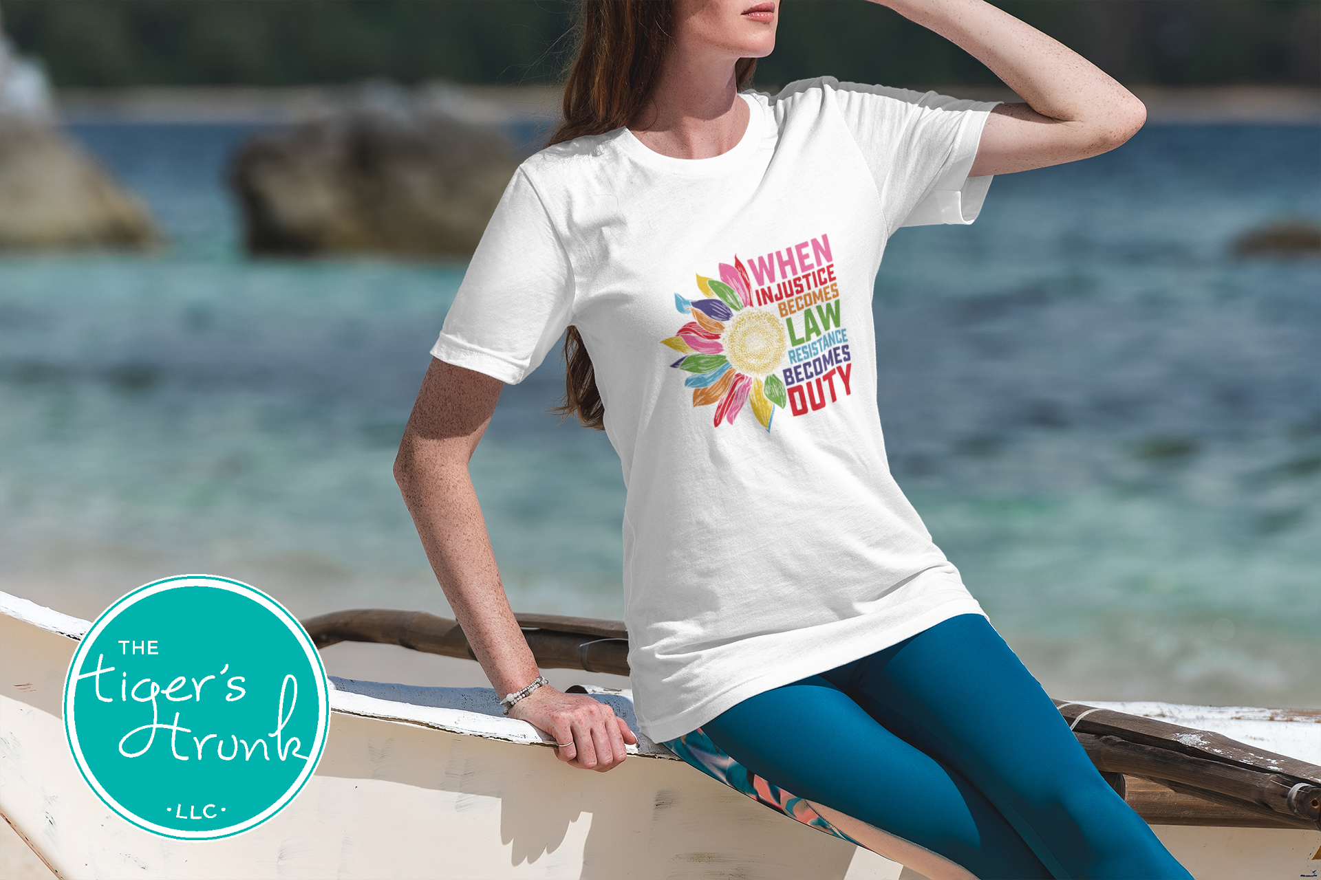 Woman wearing a white t-shirt with colorful text and graphics on a beach, with 'The Tiger's Trunk LLC' logo.