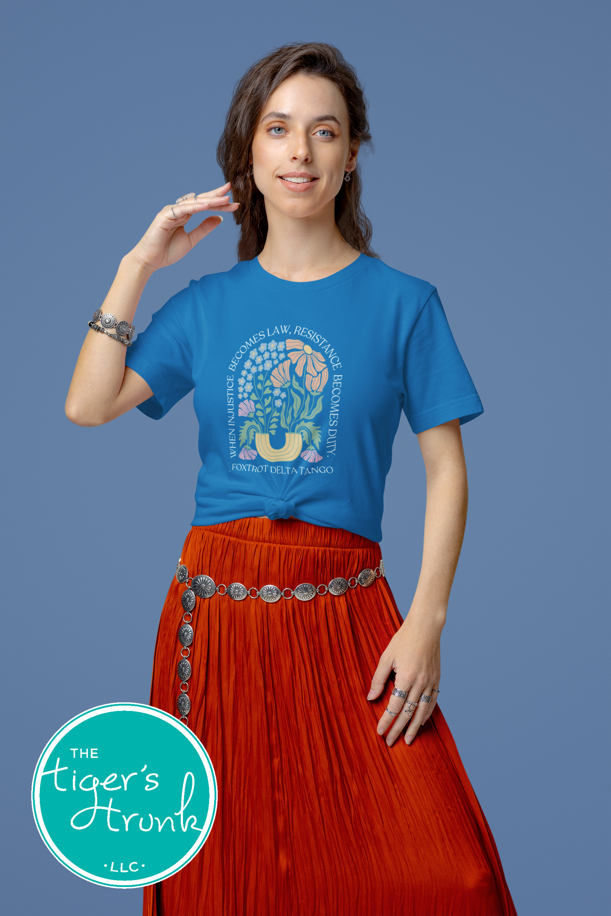 Woman wearing a blue t-shirt with a graphic design and red skirt against a blue background, with 'The Tiger's Aroh' logo.