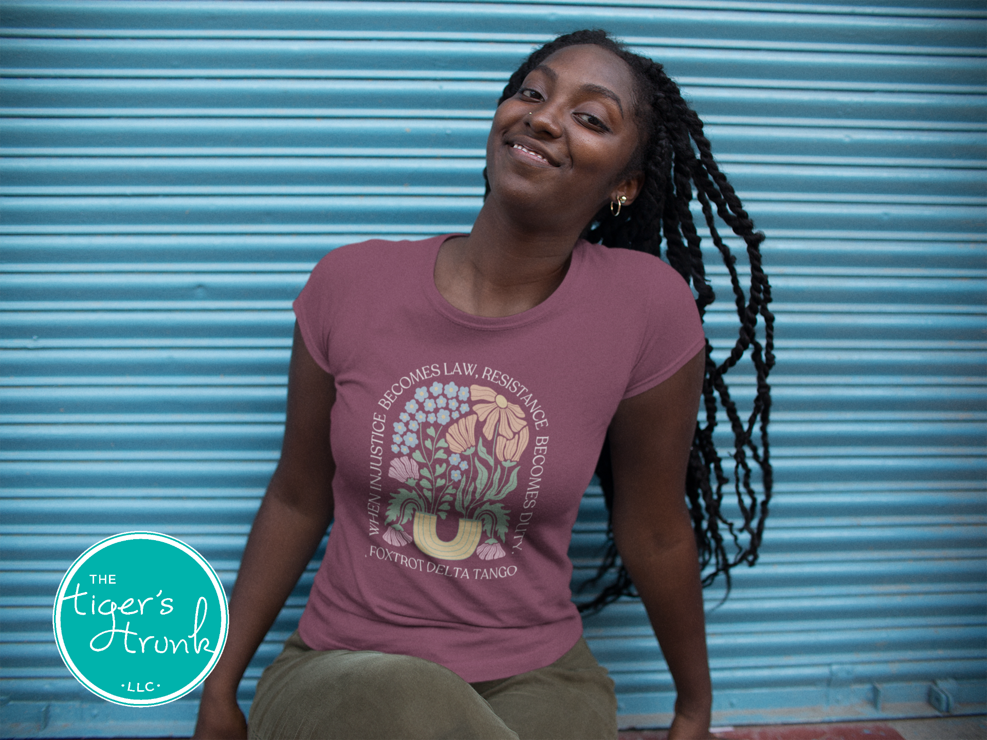 Woman wearing a pink t-shirt with a graphic design, sitting against a blue metal shutter.