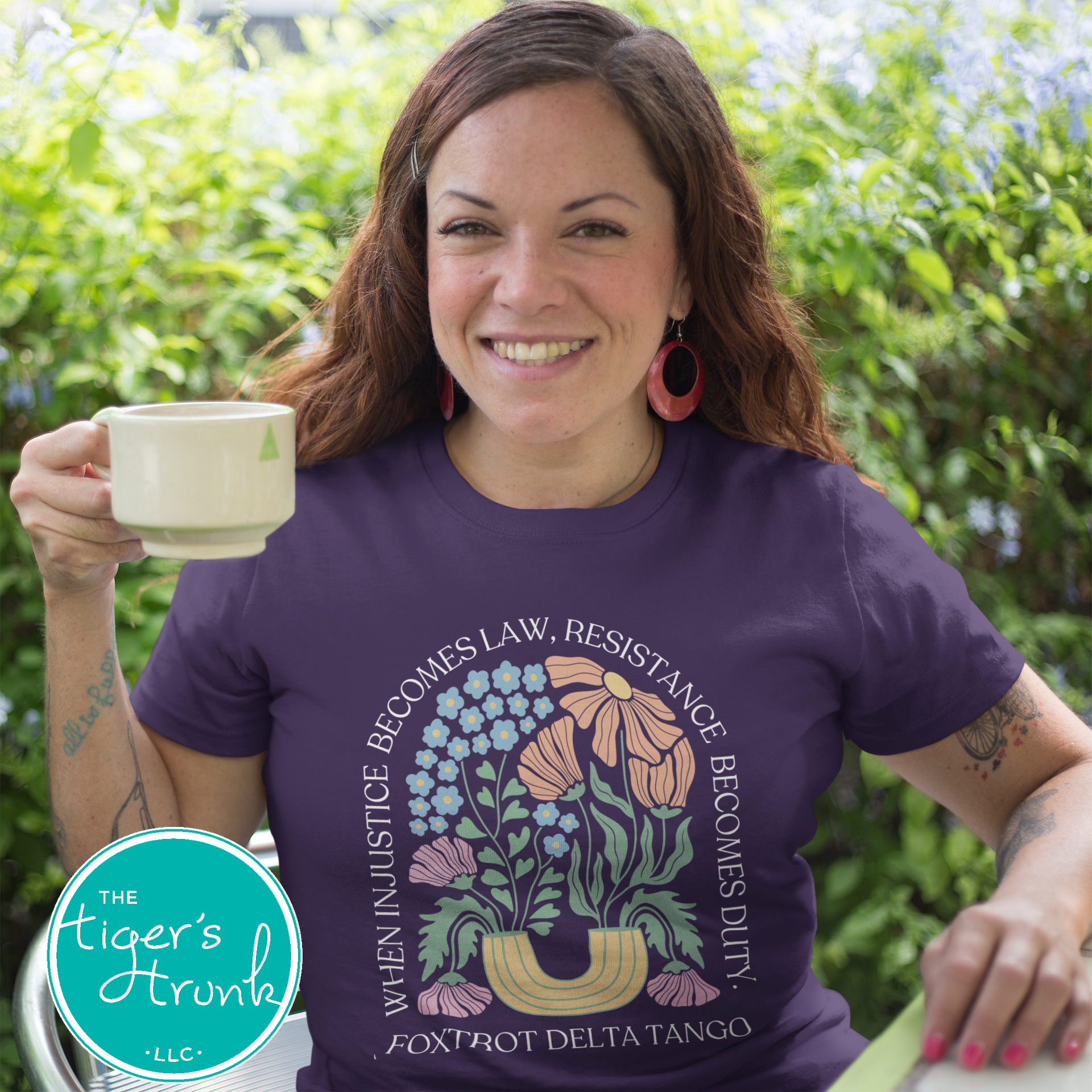 Woman wearing a purple t-shirt with a floral design and text, holding a mug outdoors.