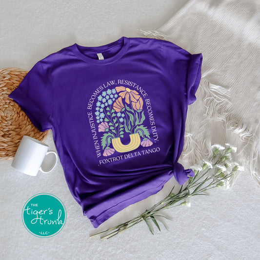Purple t-shirt with graphic design and text on a textured surface with a mug and flowers.