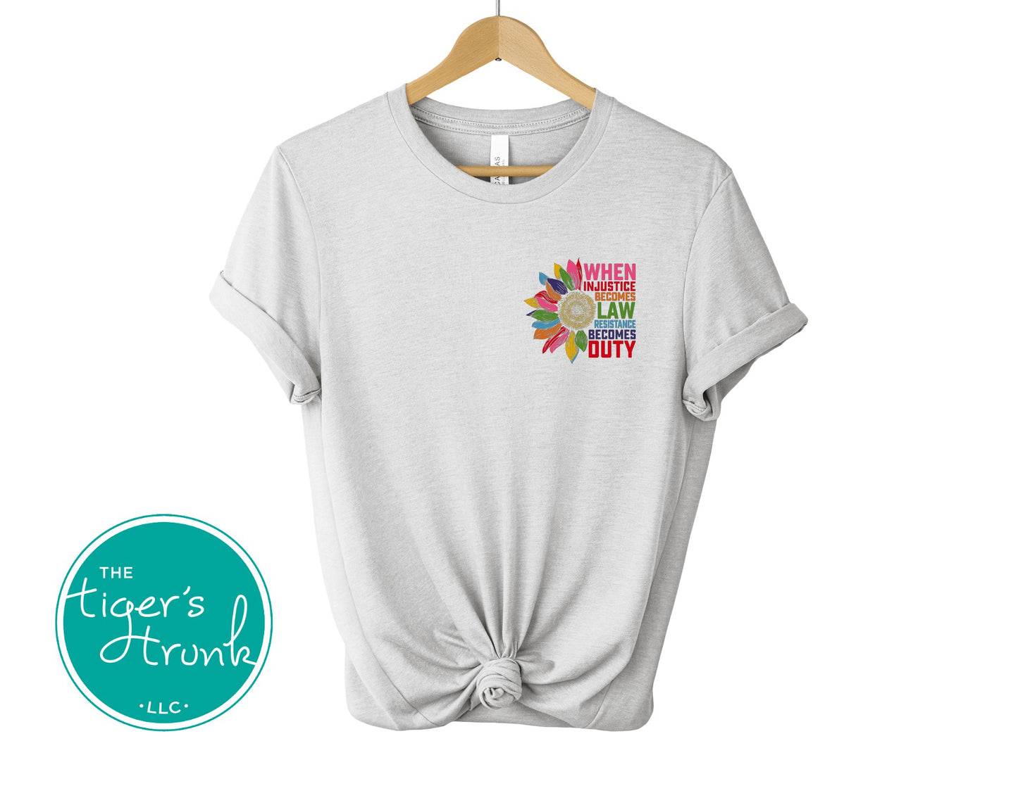 Gray t-shirt with colorful graphic and text on a hanger, branded with 'The Tiger's Trunk'.