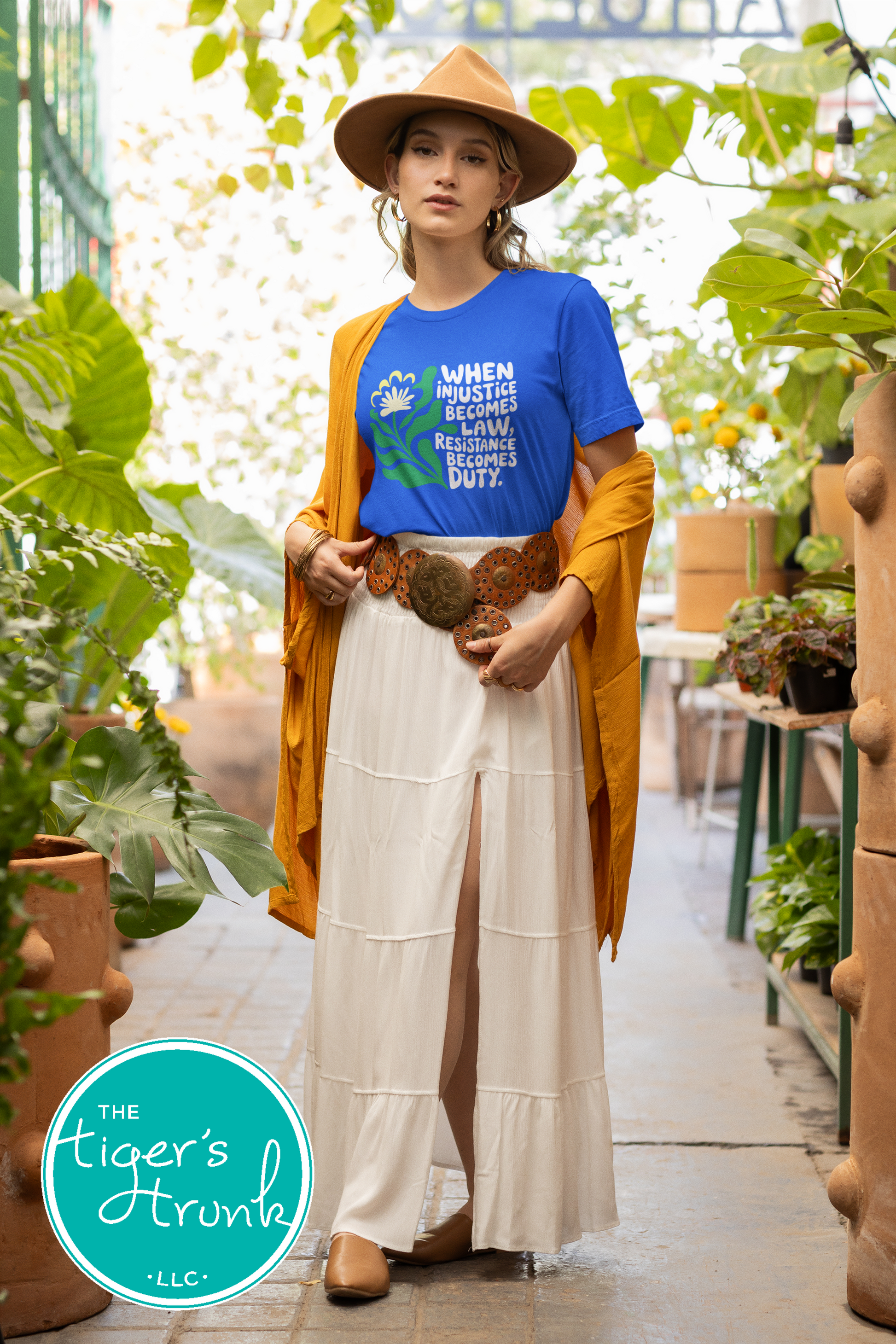 Woman in a blue t-shirt and white skirt standing in a greenhouse with plants around.