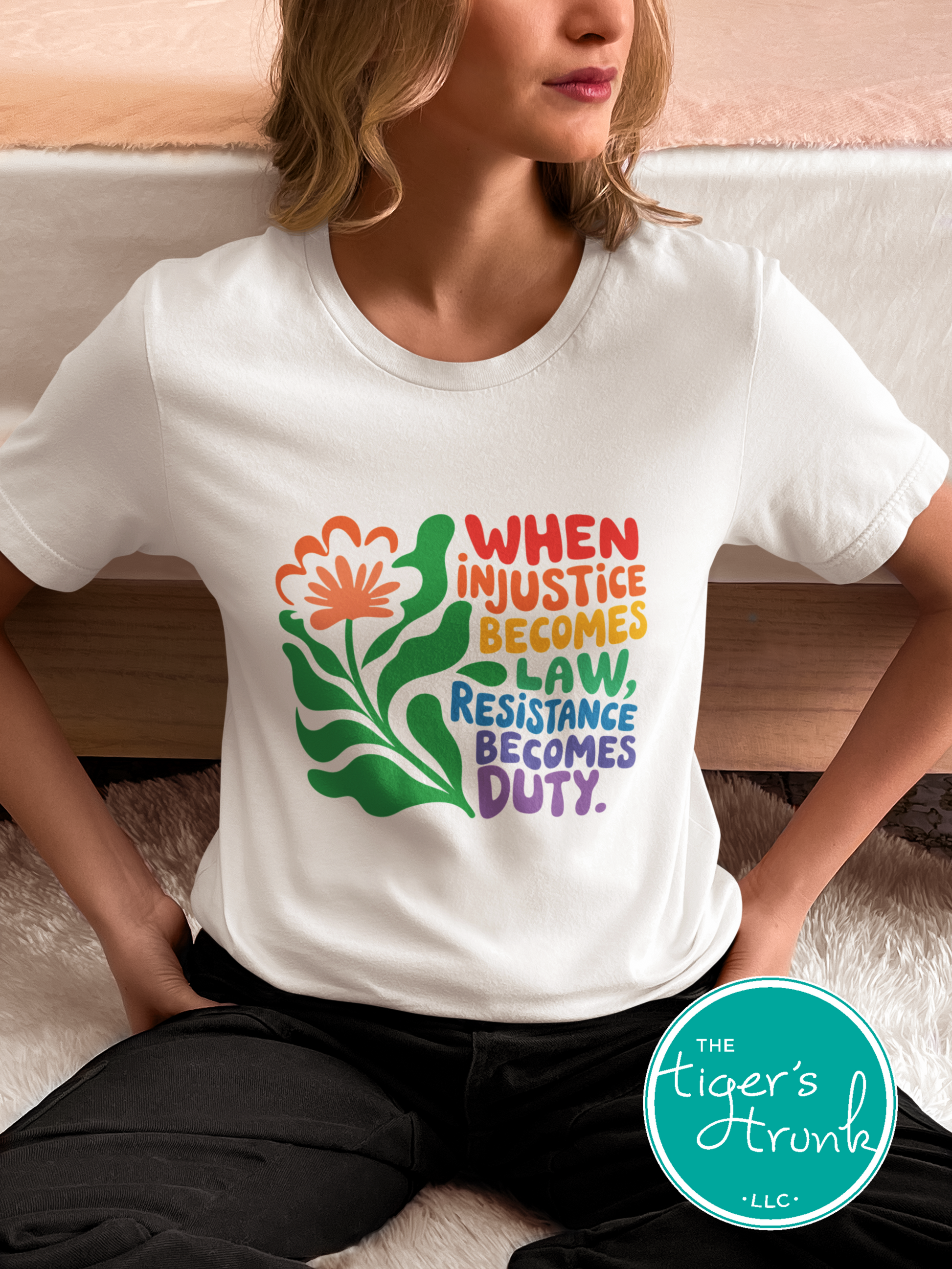 Person wearing a white t-shirt with colorful graphic and text, sitting on a couch.