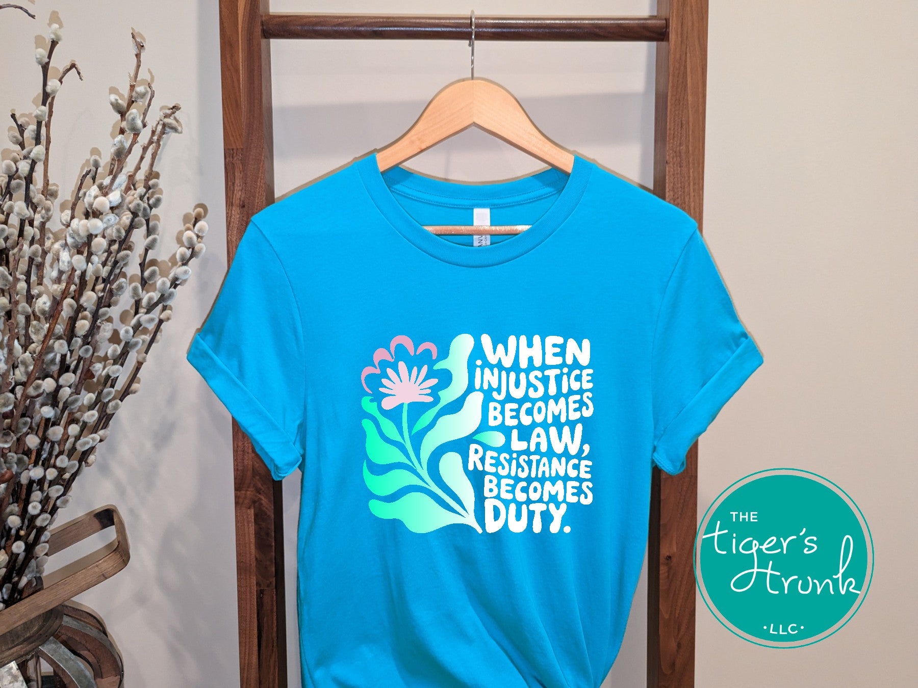 Aqua t-shirt with a motivational quote on a hanger, branded 'The Tiger's Trunk'.