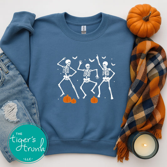 Blue sweatshirt with dancing skeletons design, surrounded by pumpkins, jeans, a plaid scarf, and a candle.