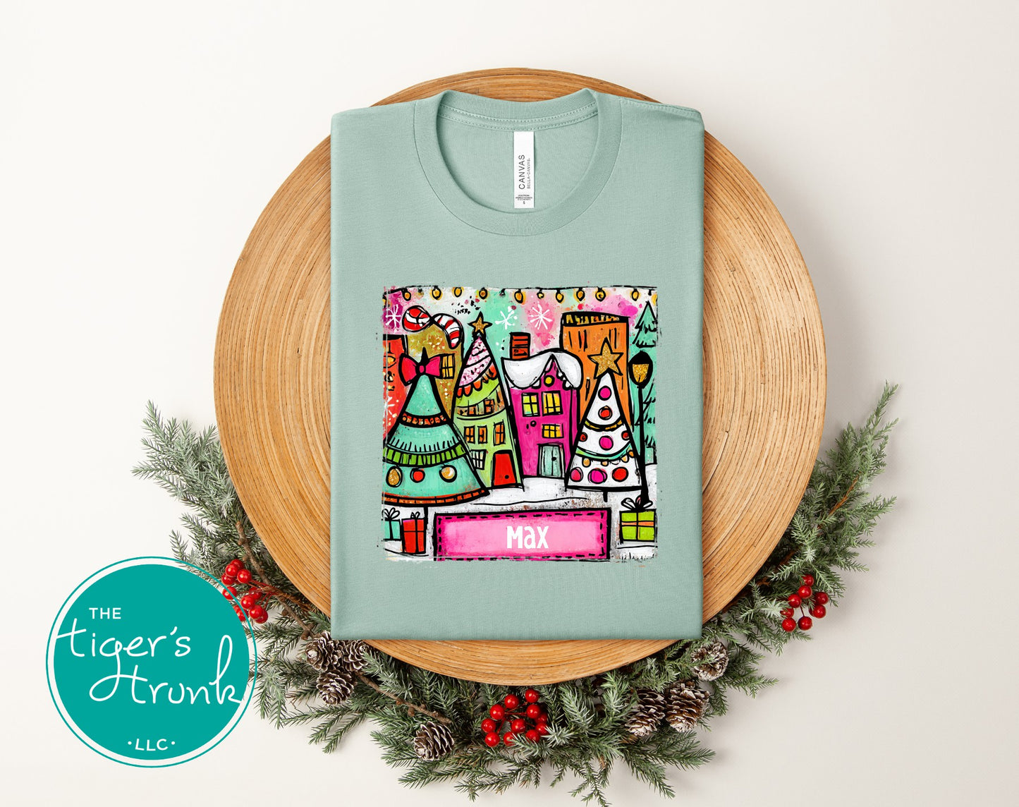 Light blue t-shirt with colorful graphic design on a wooden board with Christmas decorations.