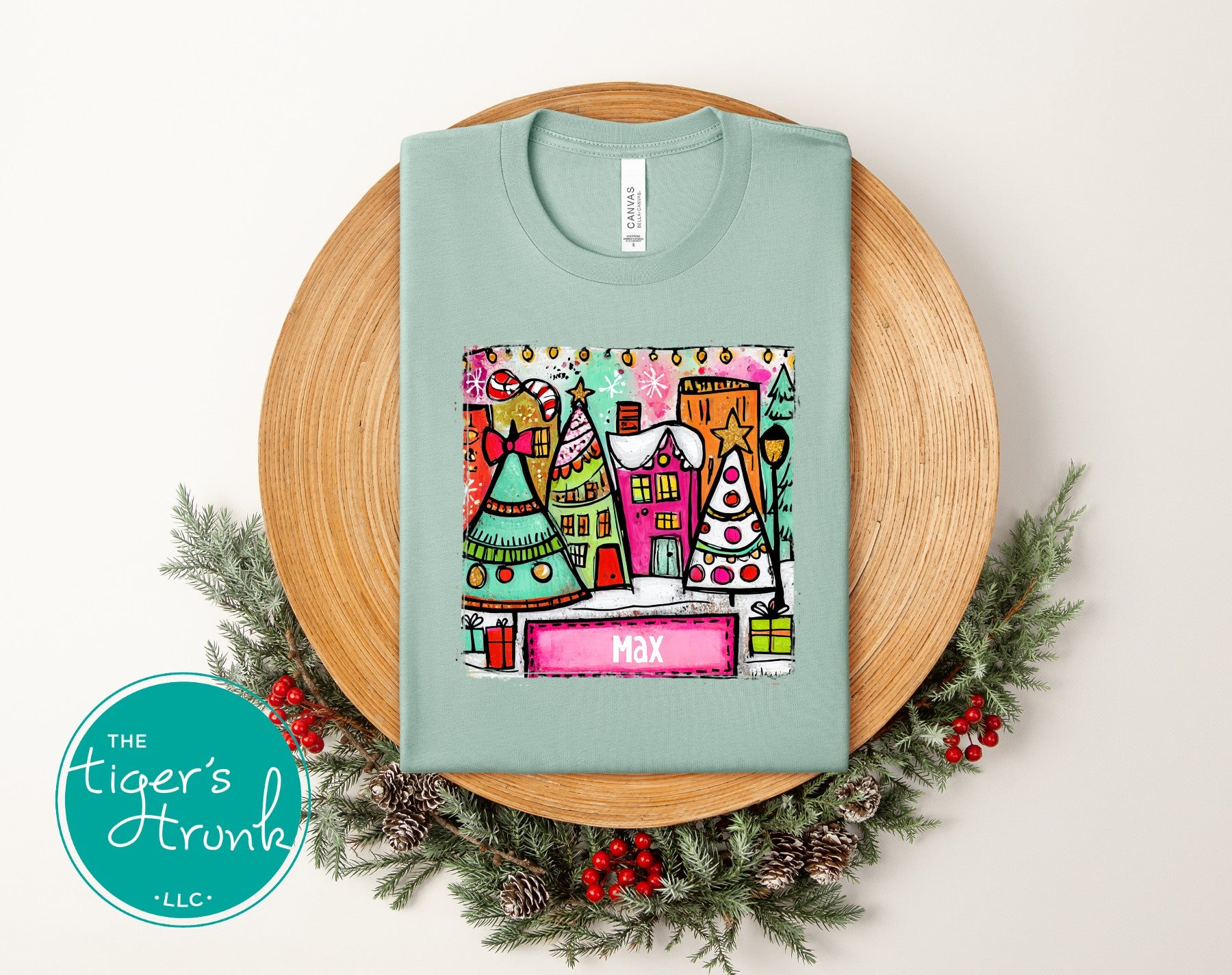 Light blue t-shirt with colorful graphic design on a wooden board with Christmas decorations.