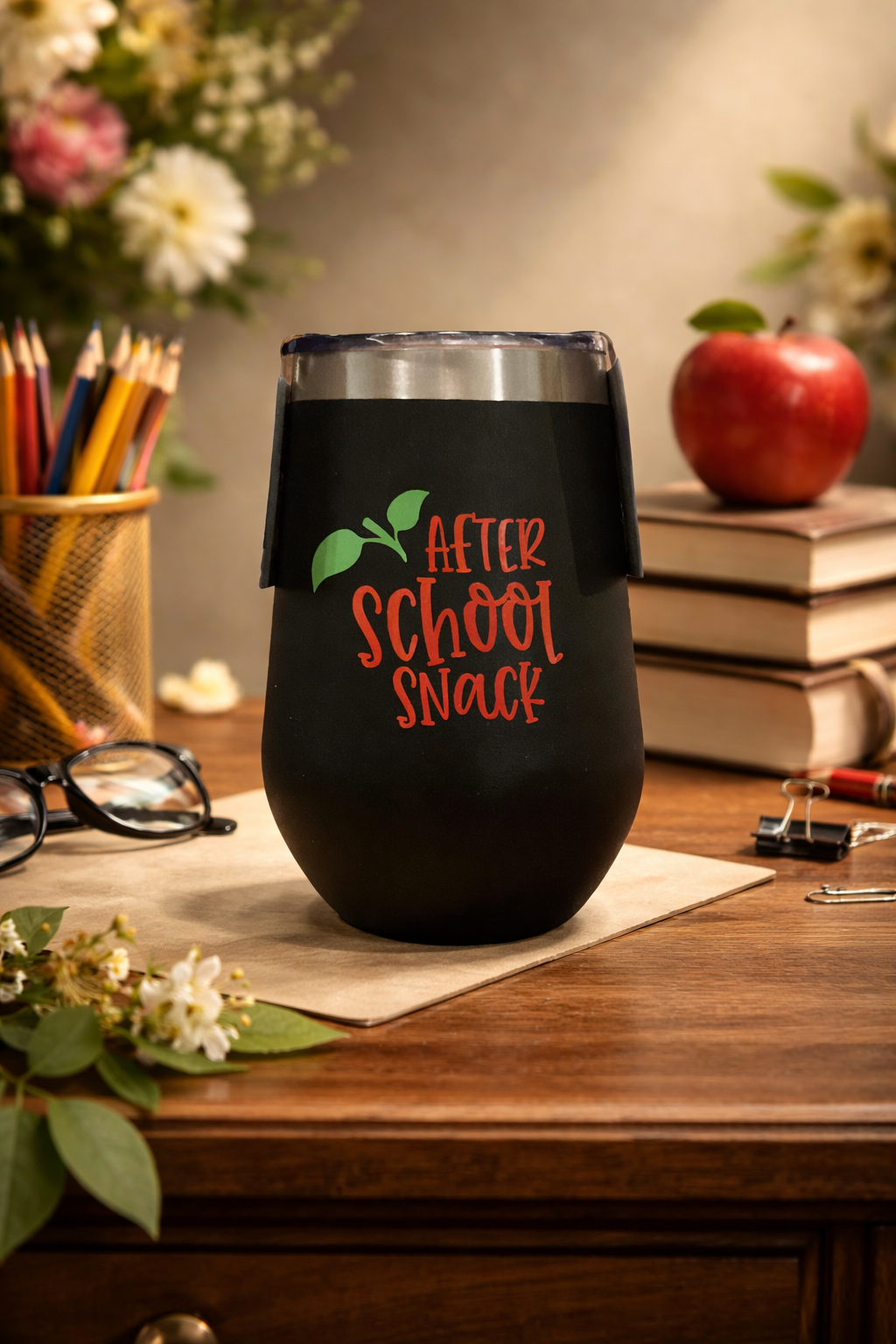 Black tumbler with 'After School Snack' text on a wooden surface with books and an apple.