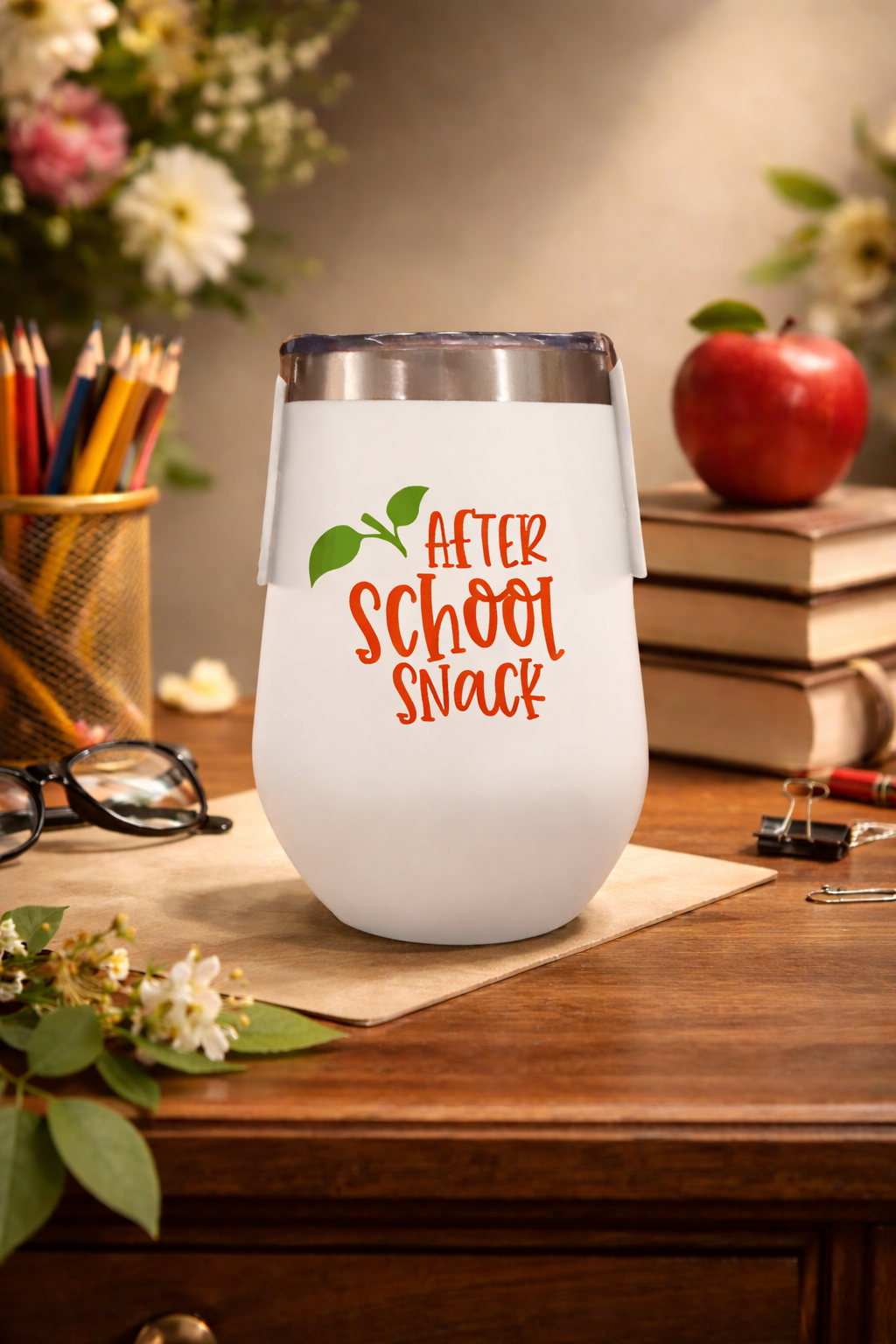 White tumbler with 'After School Snack' text on a wooden desk with books, pencils, and an apple.