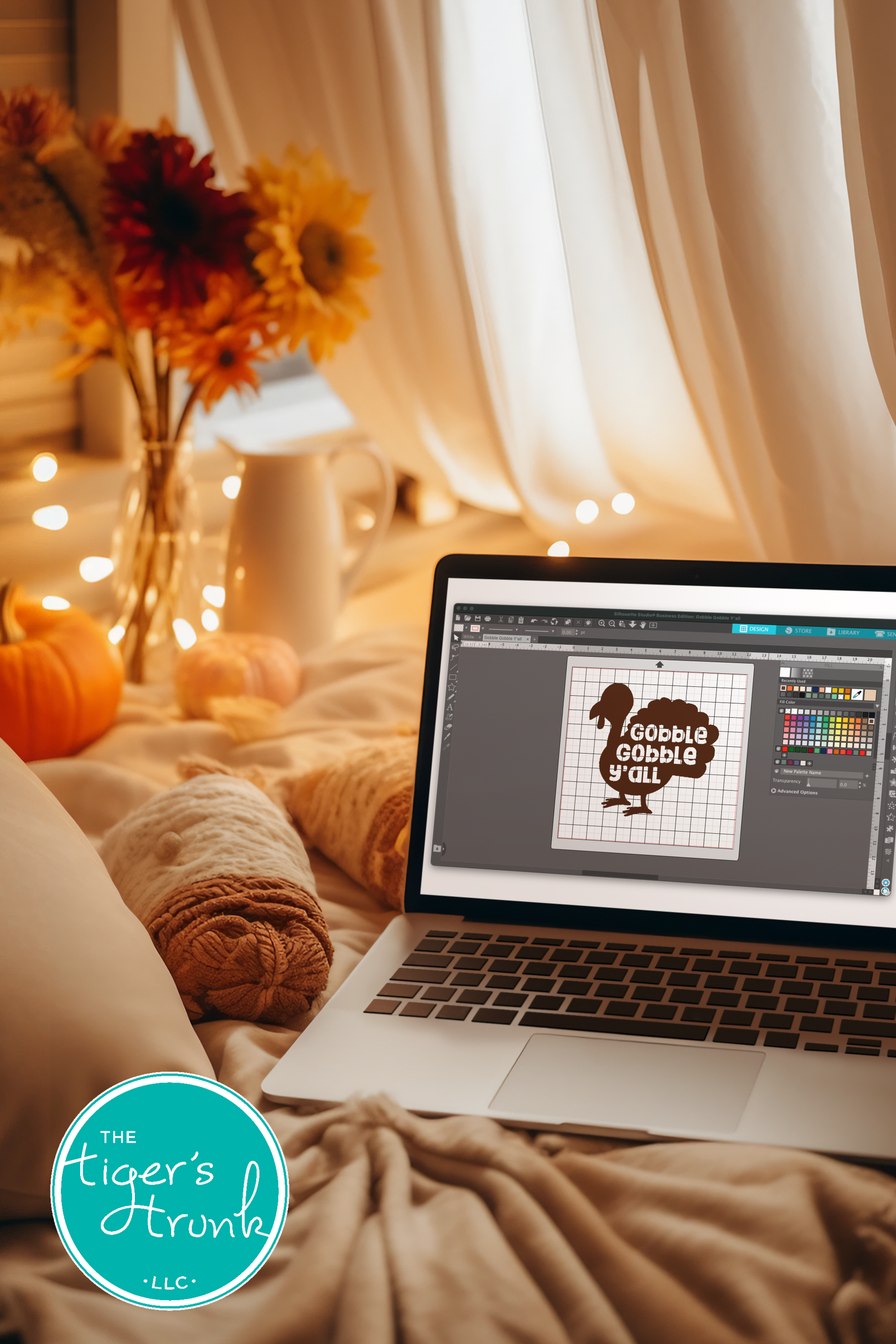 Laptop on a bed with a design software open, surrounded by autumn decorations.