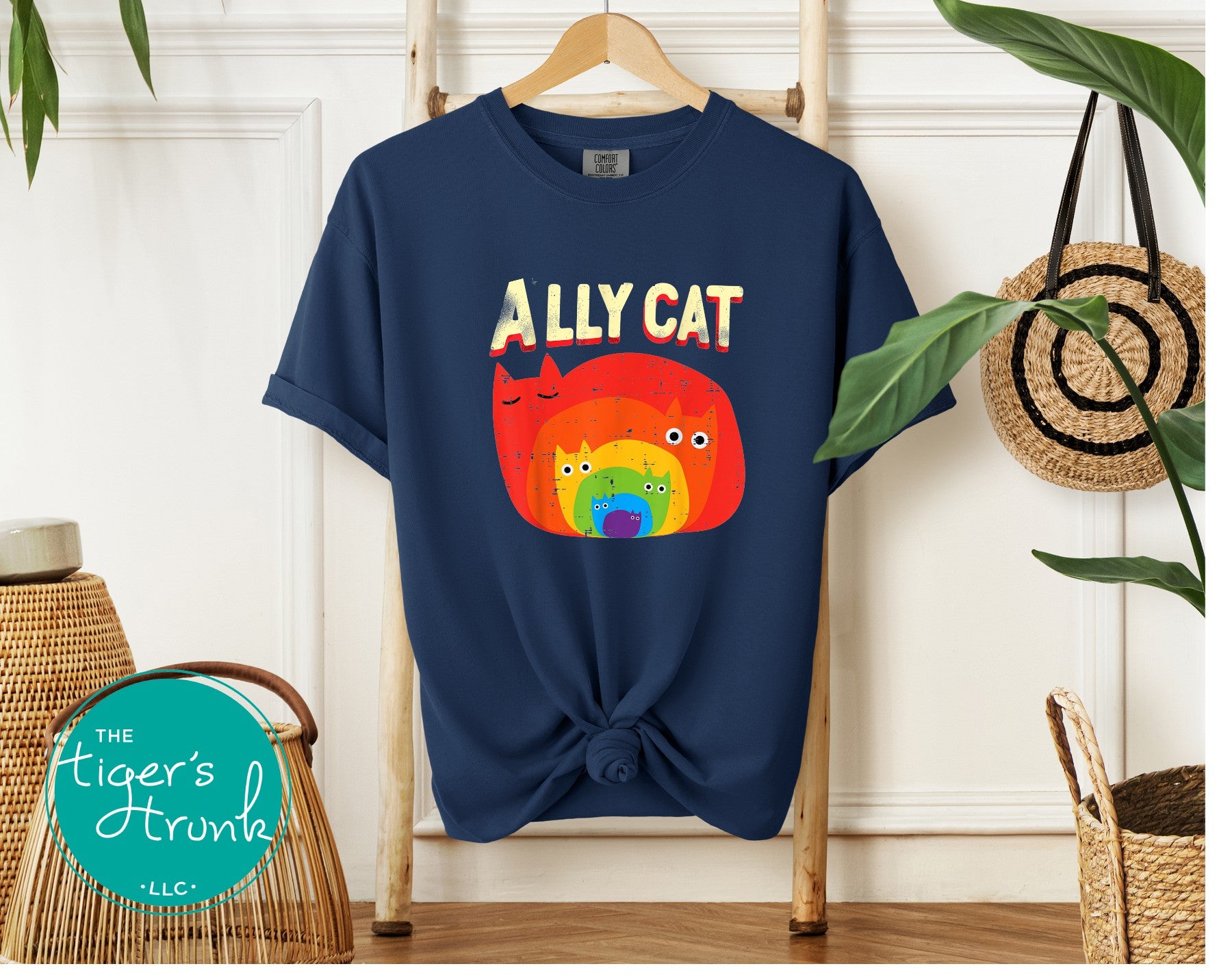 Navy blue t-shirt with colorful 'ALLY CAT' design on a hanger against a white wall.
