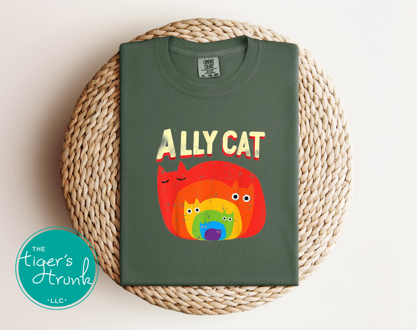 Green t-shirt with colorful 'ALLY CAT' design on a woven mat, featuring 'The Tiger's Trunk' logo.
