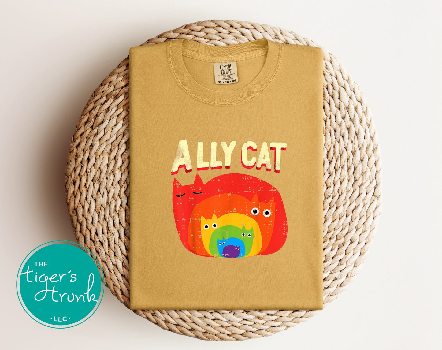 Beige t-shirt with colorful cat graphic and 'ALLY CAT' text on a woven mat, with The Tiger's Trunk logo.