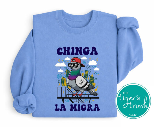 Blue sweatshirt with a graphic of a pigeon and text 'CHINGA LA MIGRA' on a white background.