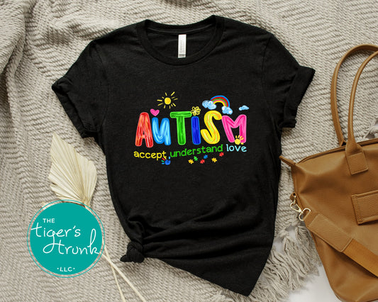 Black t-shirt with colorful 'AUTISM accept. understand. love.' text on a textured surface with a handbag.
