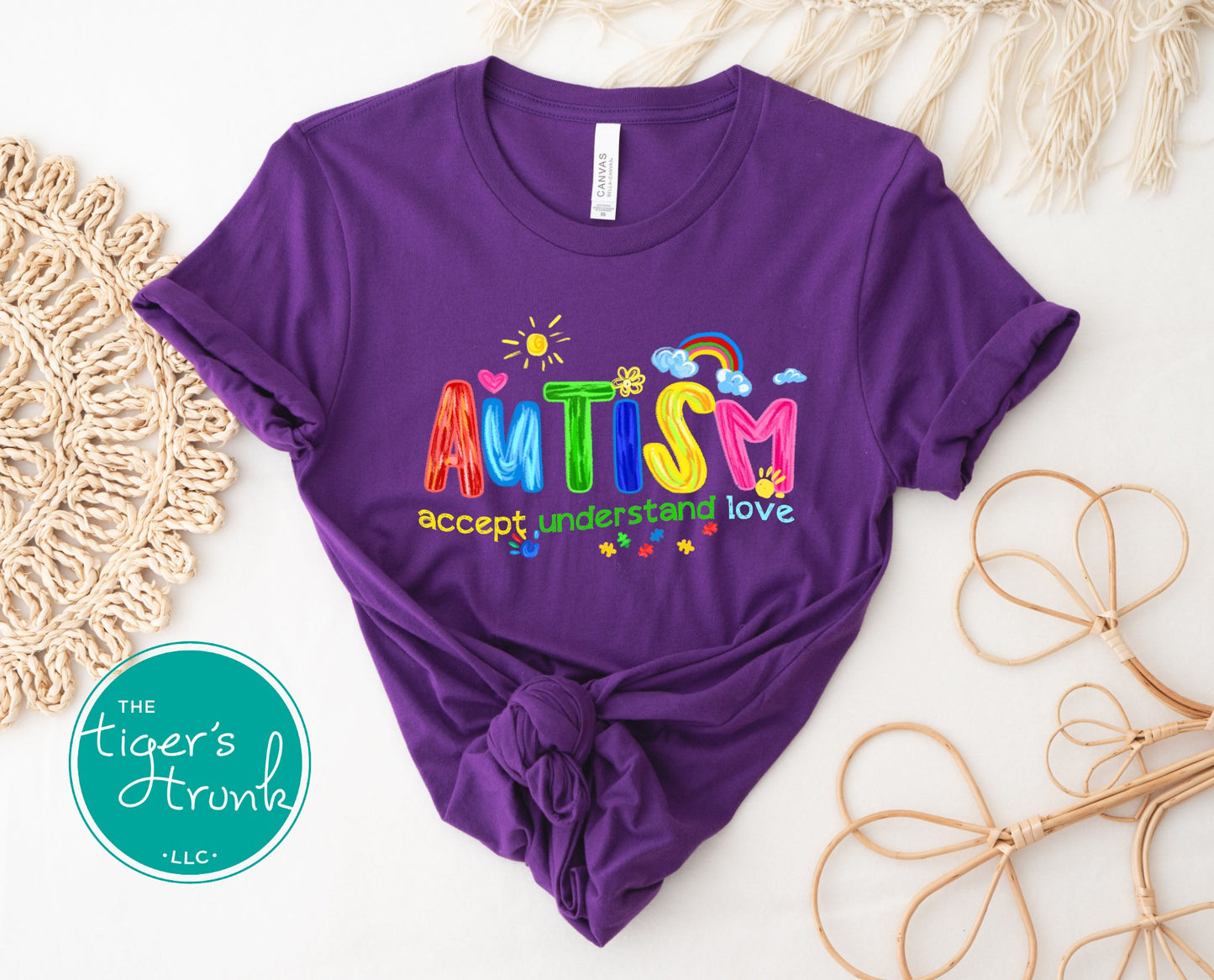 Purple t-shirt with colorful 'AUTISM accept understand love' text on a white background with decorative elements.