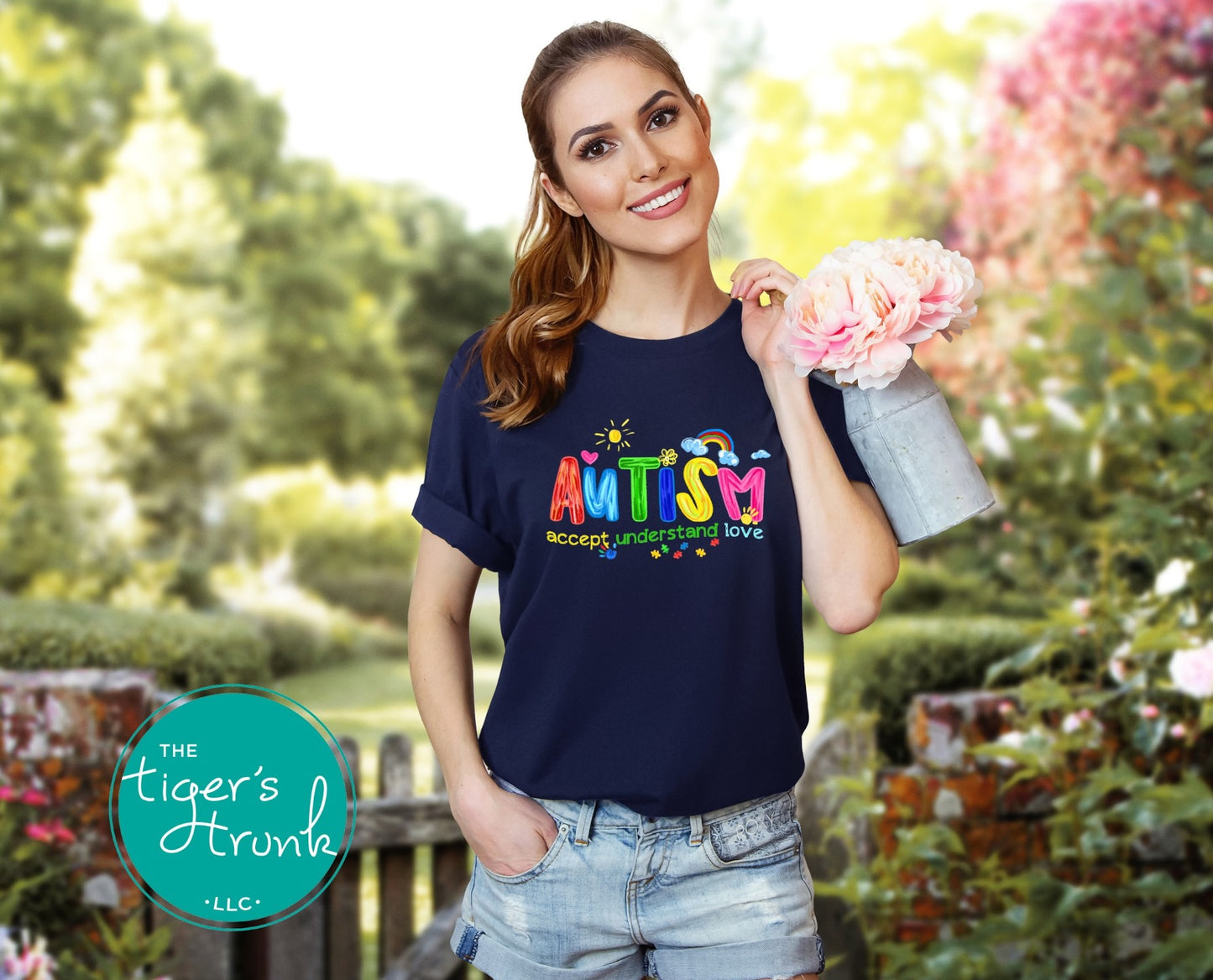 Woman wearing a navy blue t-shirt with 'Autism Accept Understand Love' text, holding flowers in a garden setting.