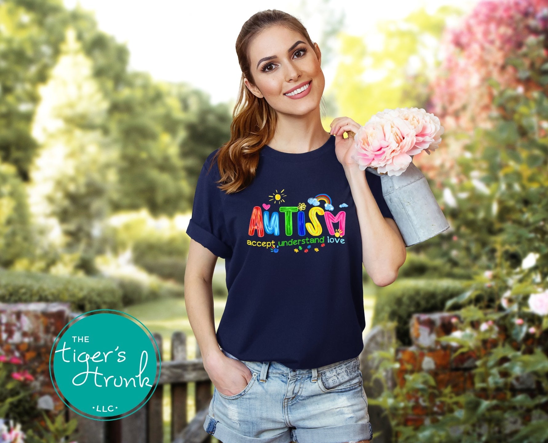Woman wearing a navy blue t-shirt with 'Autism Accept Understand Love' text, holding flowers in a garden setting.