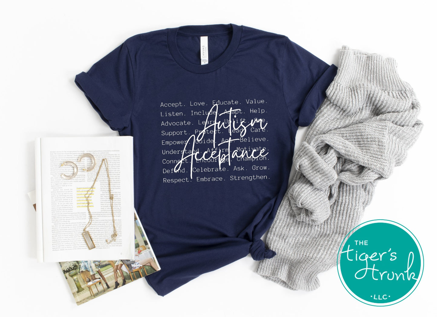 Navy t-shirt with 'Autism Acceptance' text, gray pants, and books on a white background with 'The Tiger's Trunk' logo.