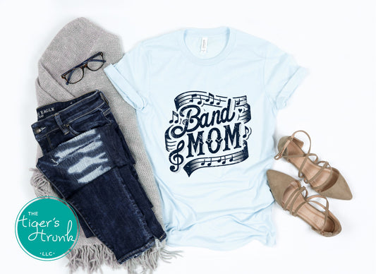 Light blue t-shirt with 'Band Mom' design, jeans, gray beanie, glasses, and beige shoes on a white background.