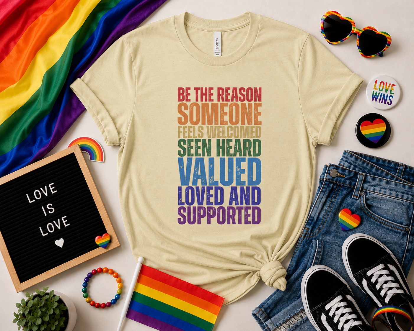 Beige t-shirt with motivational message surrounded by rainbow-themed accessories on a light background