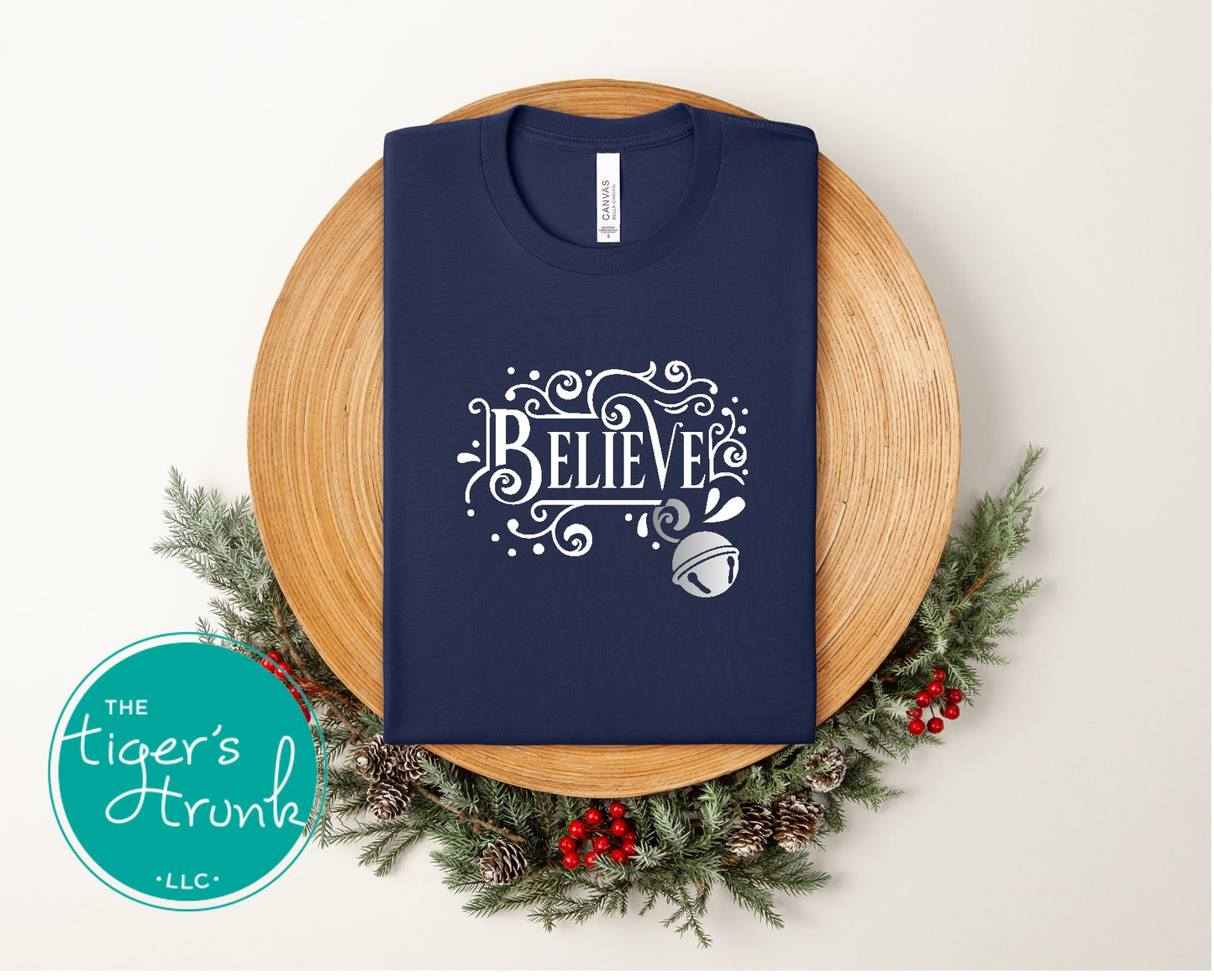 Navy blue t-shirt with 'BELIEVE' design on a wooden board with Christmas decorations