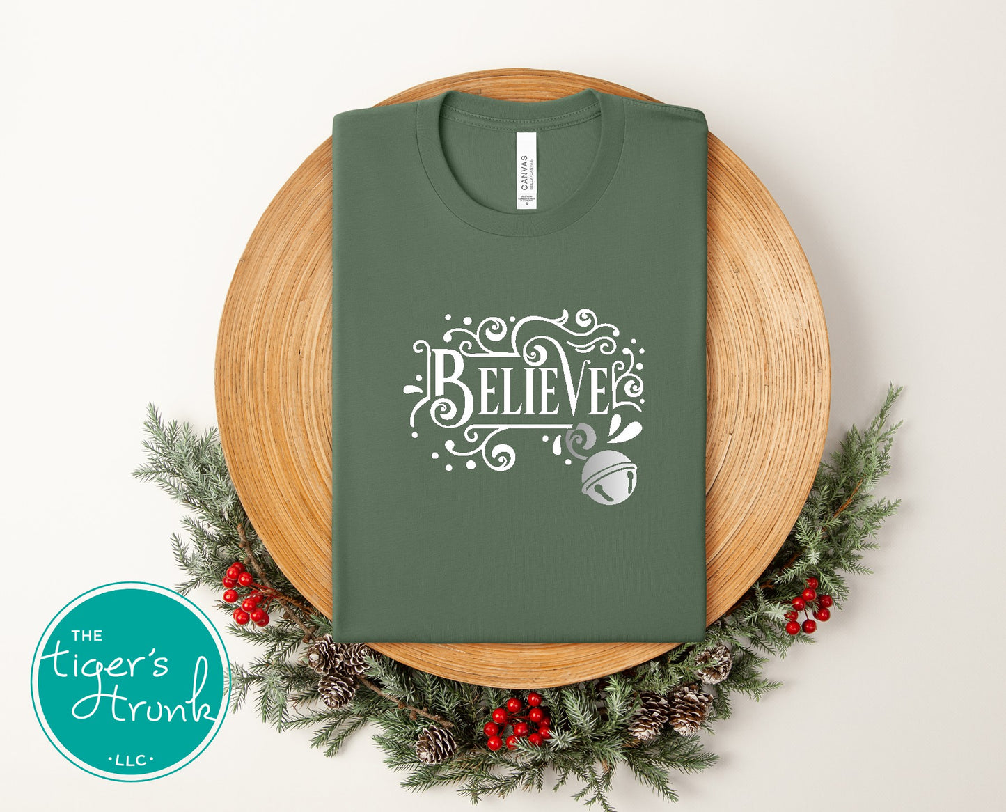 Green t-shirt with 'BELIEVE' design on a wooden plate surrounded by Christmas decorations.