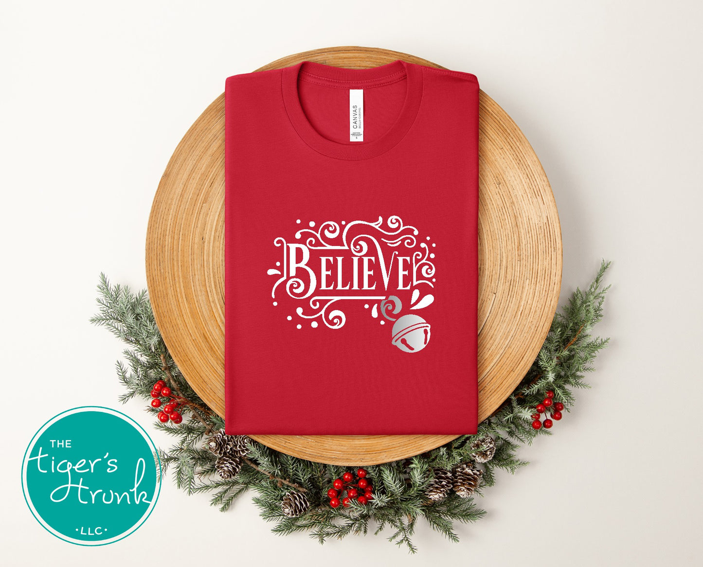 Red t-shirt with 'BELIEVE' design on a wooden surface with Christmas decorations