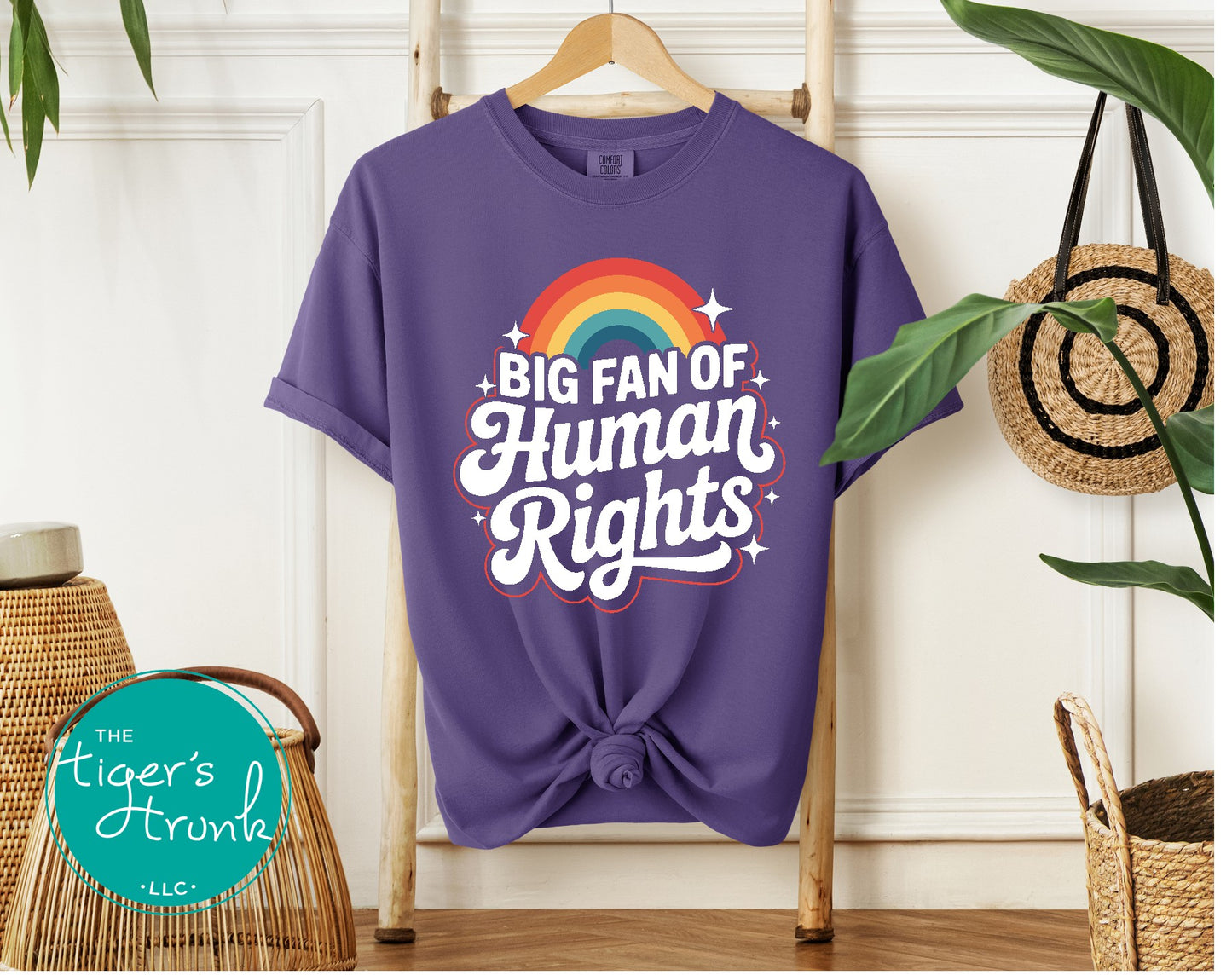 Purple t-shirt with 'Big Fan of Human Rights' text and rainbow design on a hanger.