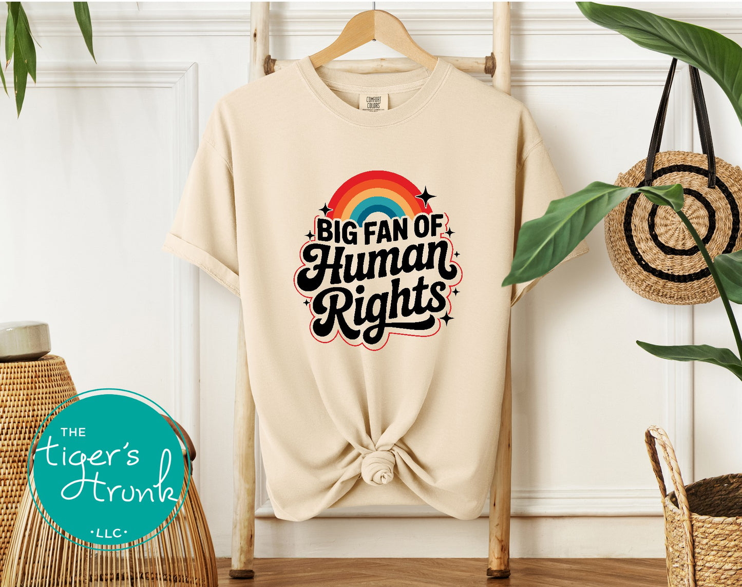 Beige t-shirt with 'Big Fan of Human Rights' text and rainbow design on a hanger.