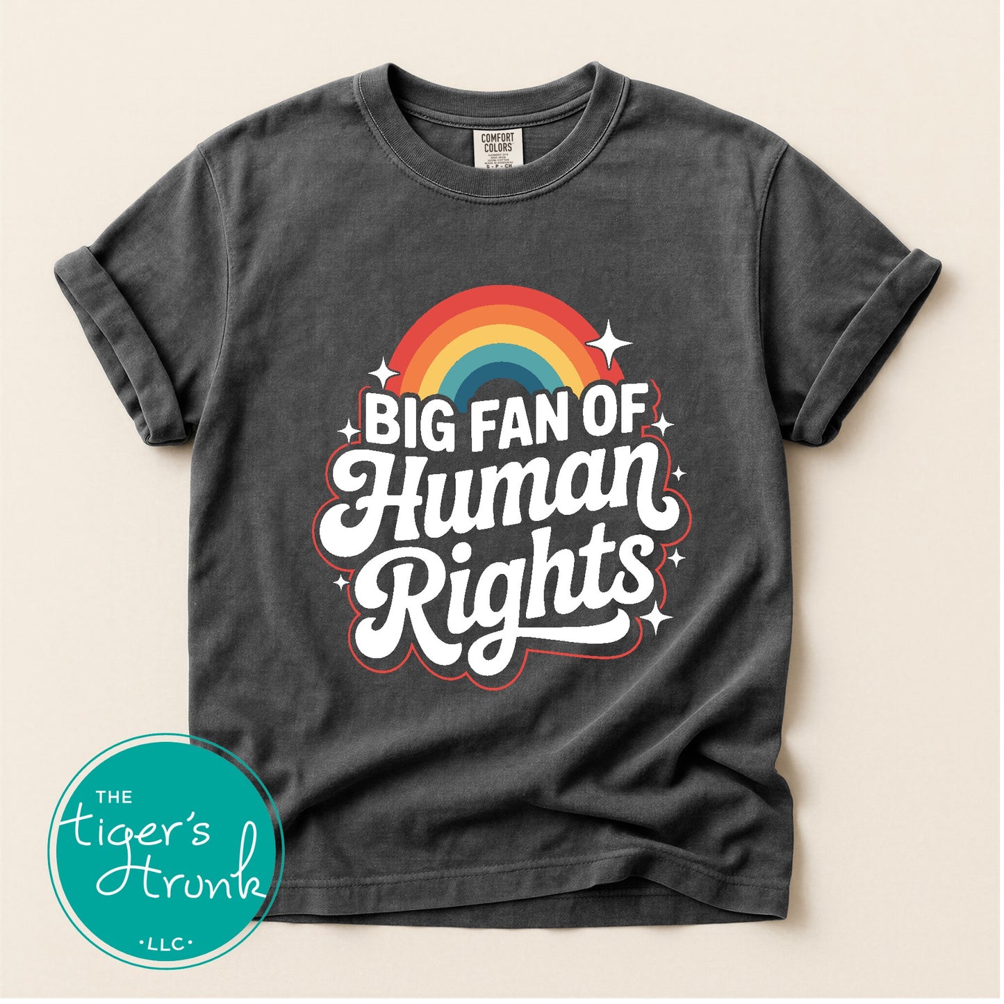 Dark gray t-shirt with rainbow and 'Big Fan of Human Rights' text on a beige background, featuring the brand 'The Tiger's Trunk'.