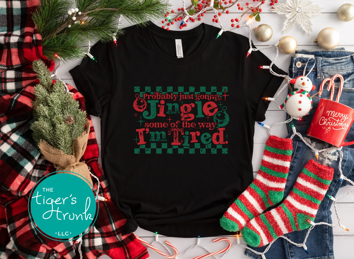 Black t-shirt with Christmas-themed text, surrounded by festive items like socks and lights.
