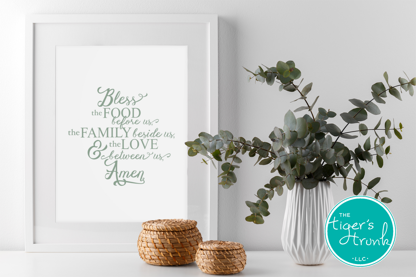Framed print with a prayer, eucalyptus plant, and woven baskets on a white surface.