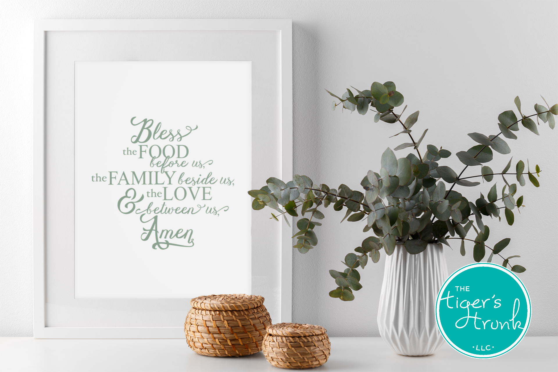 Framed print with a prayer, eucalyptus plant, and woven baskets on a white surface.