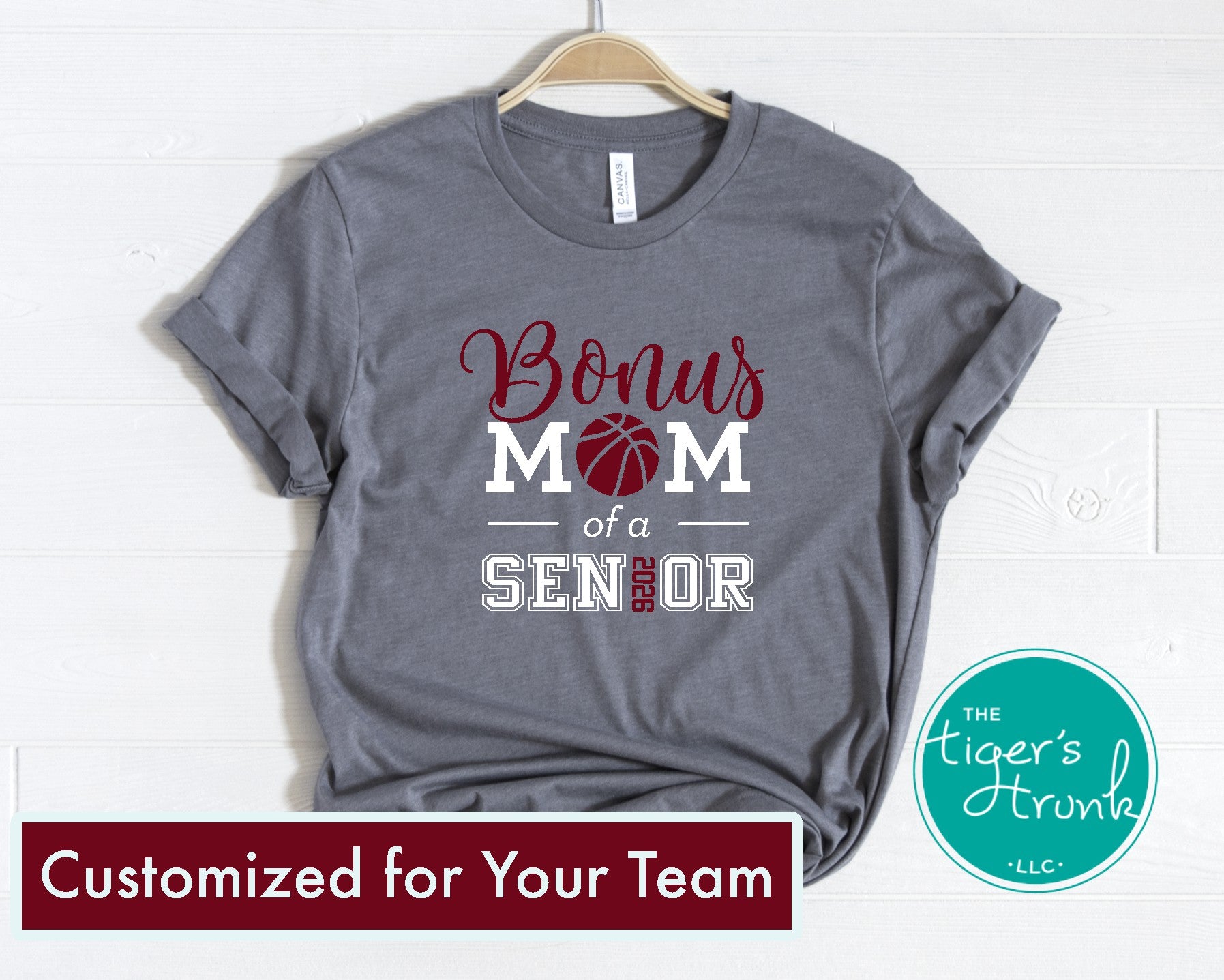 Gray t-shirt with 'Bonus Mom of a Senior' text on a hanger, branded with 'The Tiger's Trunk'.
