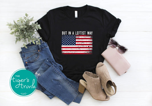 Black t-shirt with American flag graphic and text, paired with jeans, boots, sunglasses, and a plant on a white background.