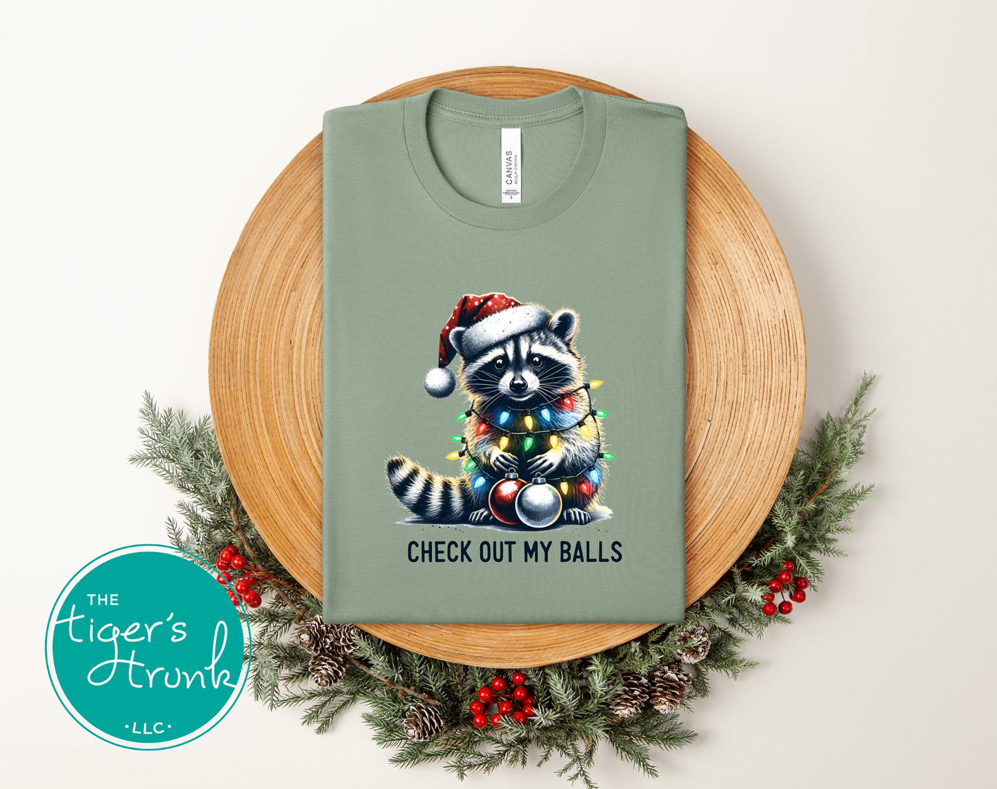 Green t-shirt with a raccoon design and text on a wooden board with Christmas decorations.