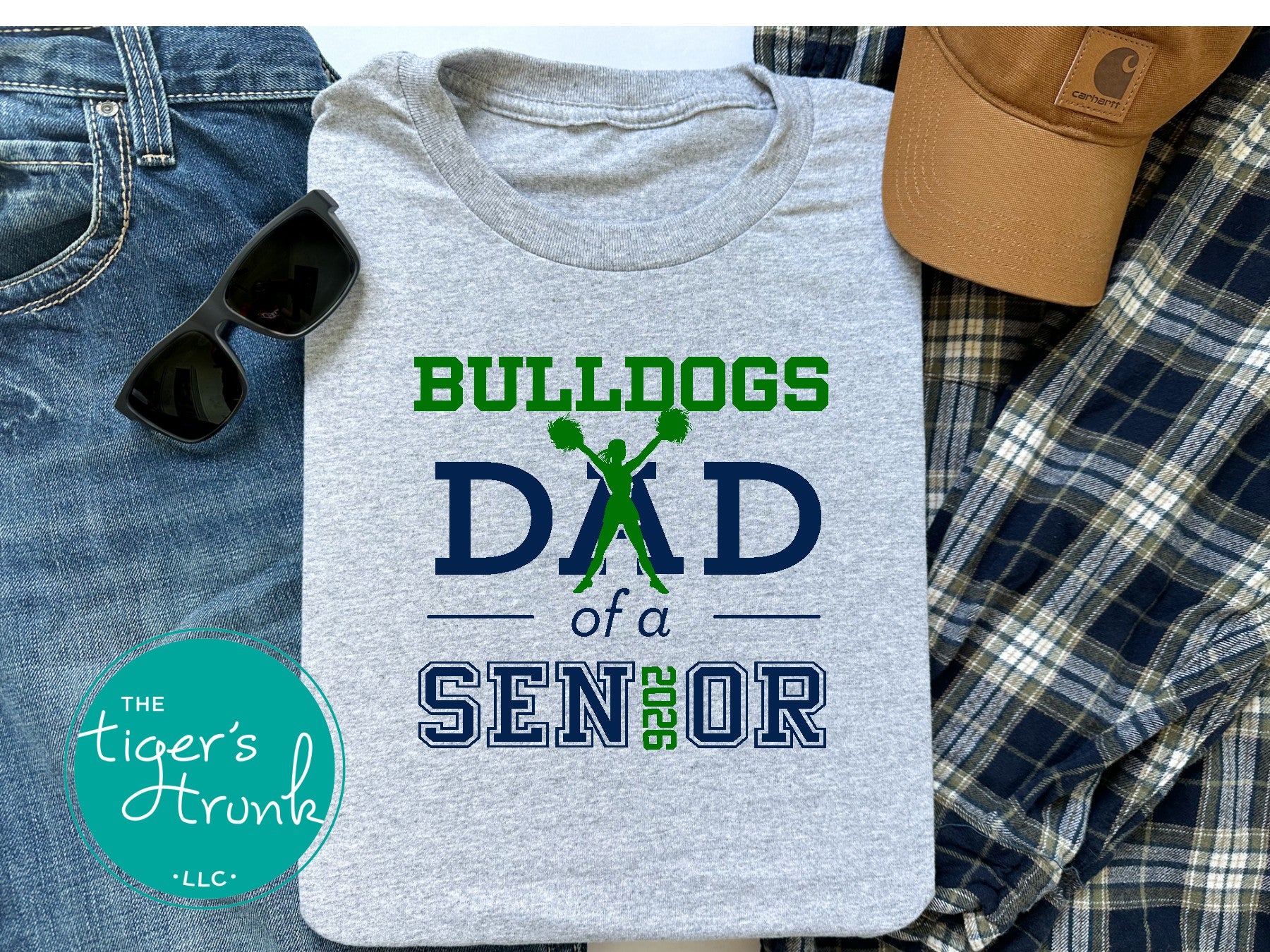 Gray t-shirt with 'Bulldogs Dad of a Senior' design on a surface with jeans, sunglasses, and a cap.