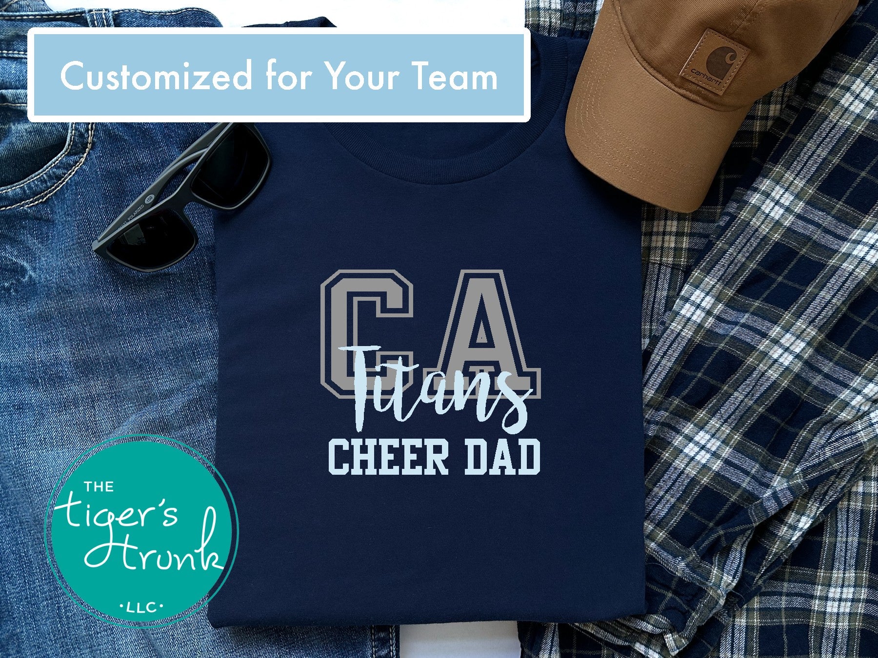 Navy t-shirt with 'CA Titans Cheer Dad' text, sunglasses, jeans, and a cap on a checkered fabric background.