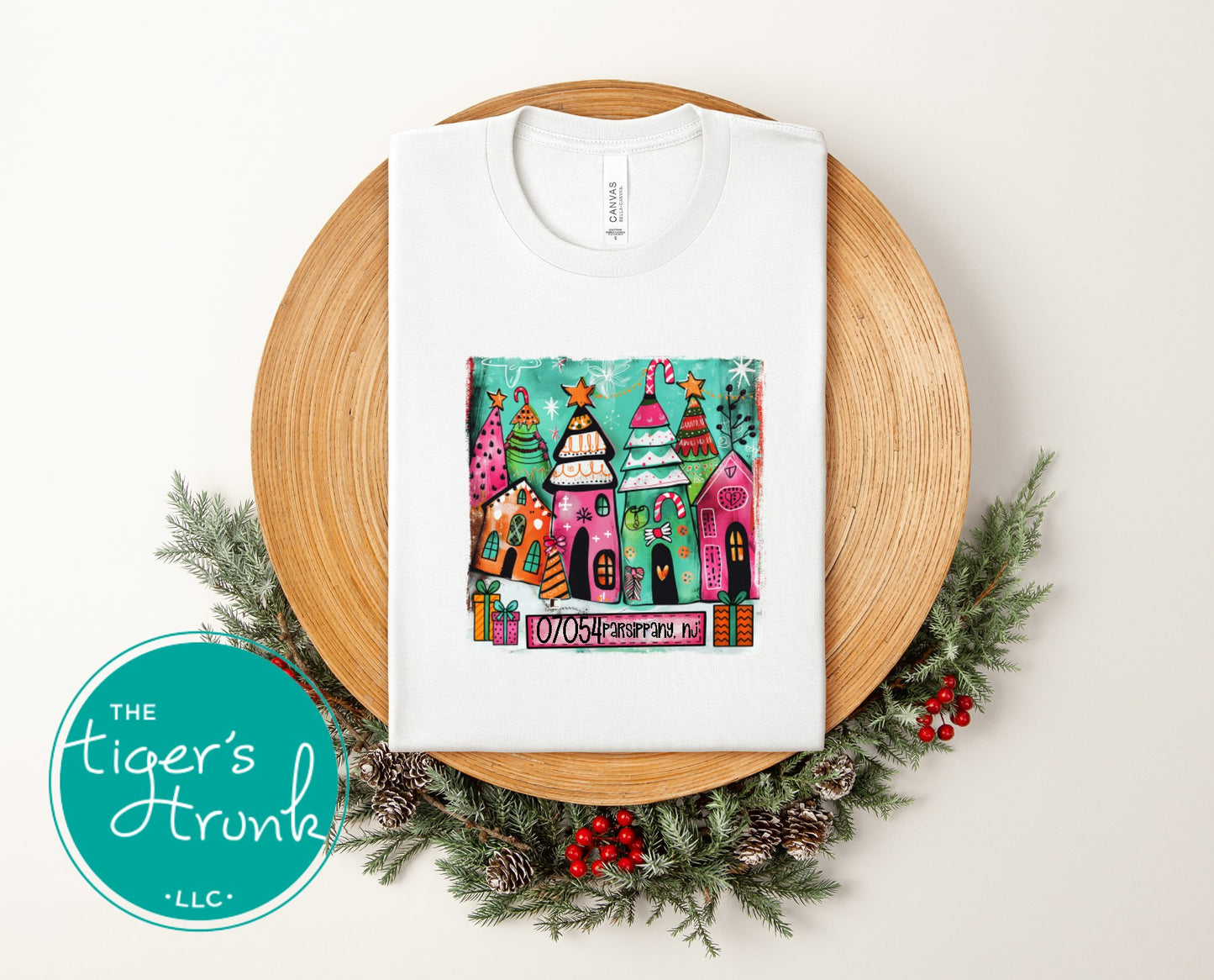 A white Christmas t-shirt featuring colorful whimsical holiday houses personalized with ZIP code 07054 Parsippany, NJ, displayed on a wooden tray with festive greenery.