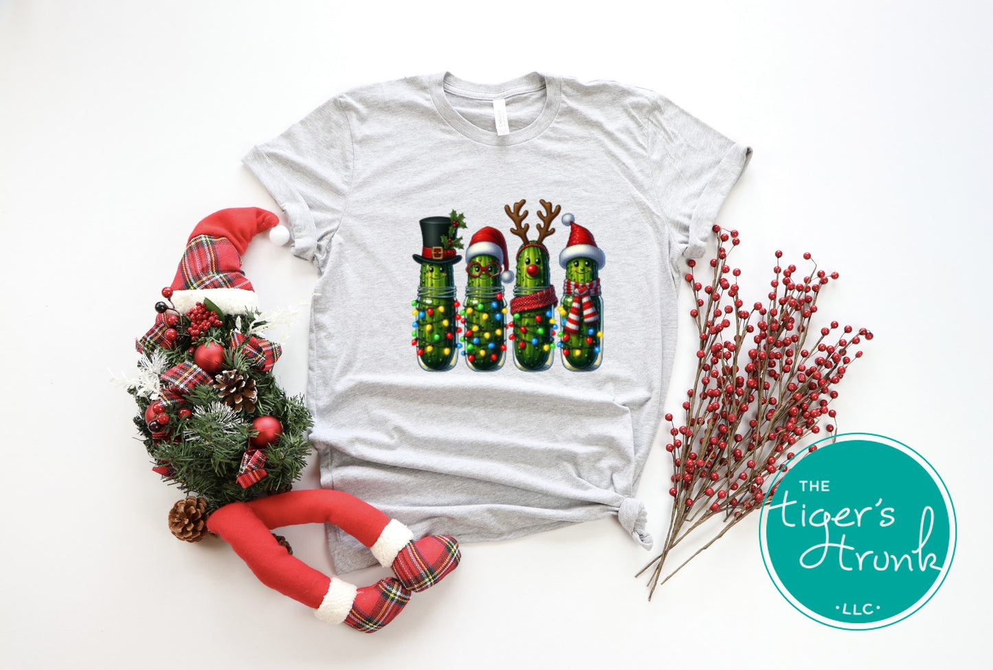 Gray t-shirt with Christmas pickle design, surrounded by festive decorations on a white background.