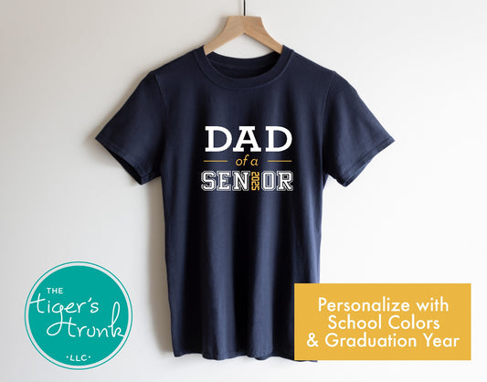 A navy blue short-sleeve t-shirt with the text 'DAD OF A SENIOR' personalized with a graduation year, displayed on a wooden hanger.